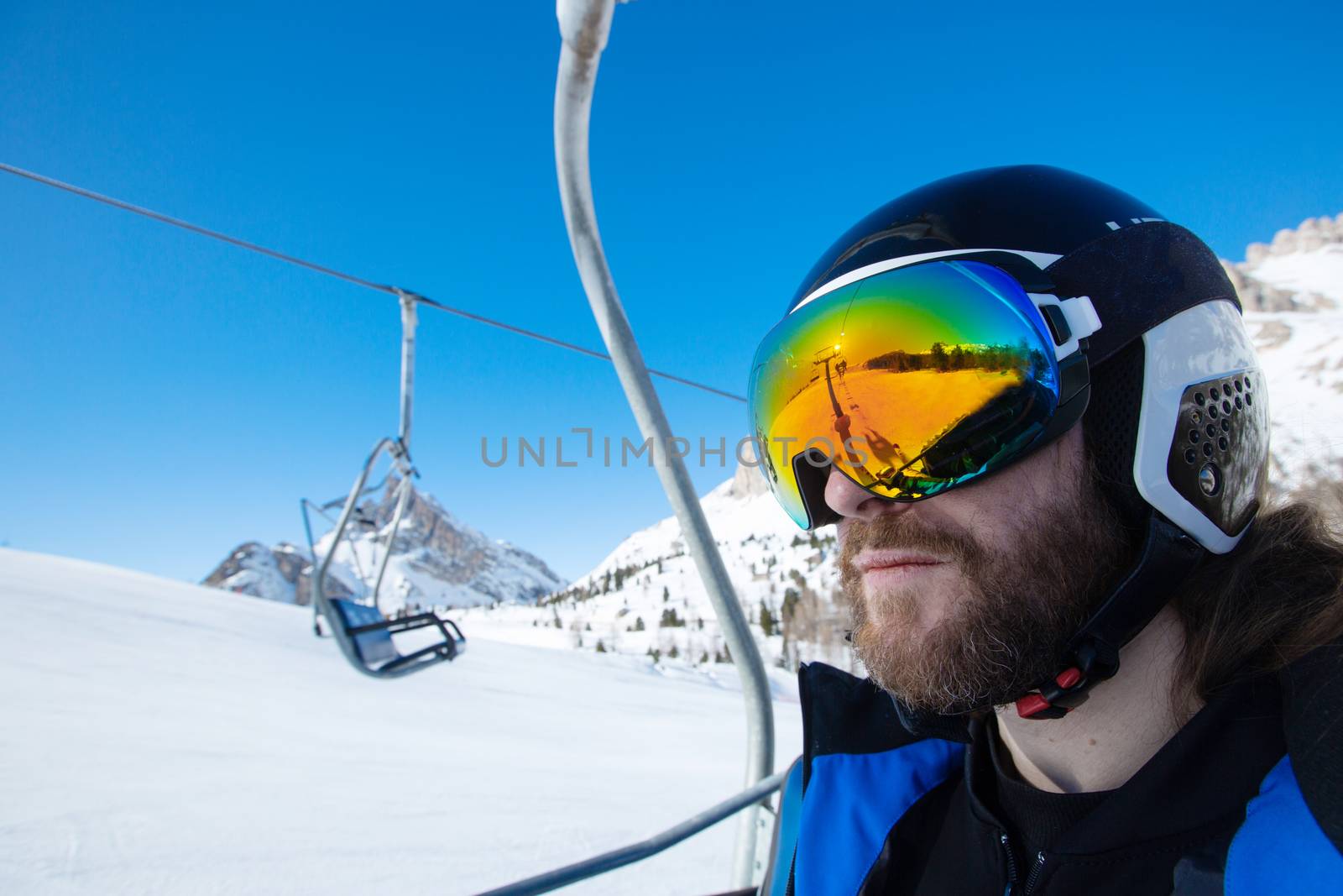 Bearded mid adult man skier in pretextive goggles and helmet sitting in ski lift at resort in Alps