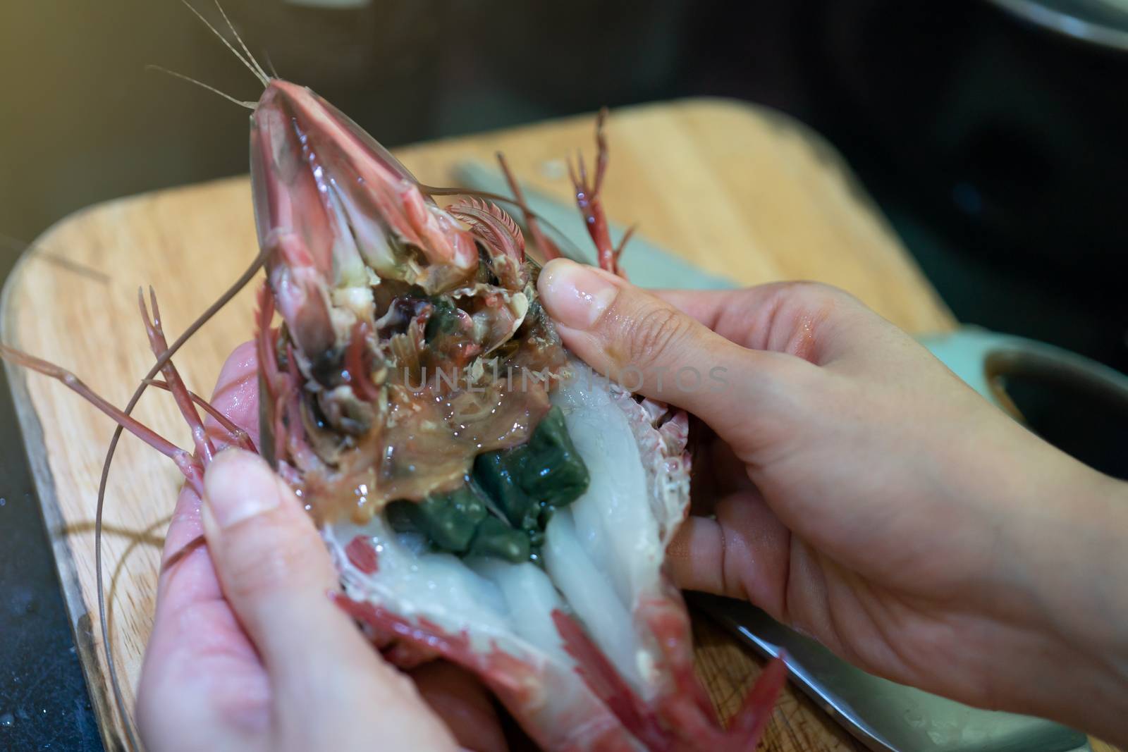 Woman hand cut in half fresh raw tiger prawn and spiny lobster by scissors.