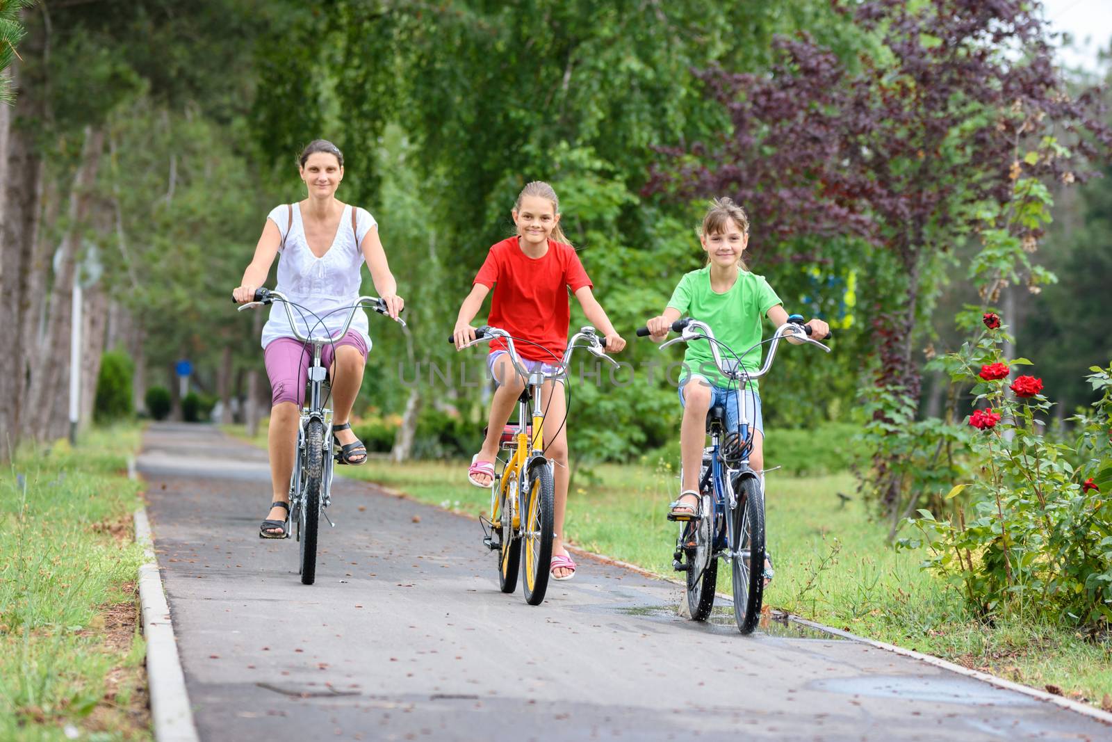Mom with two children ride a bike in the park in the morning