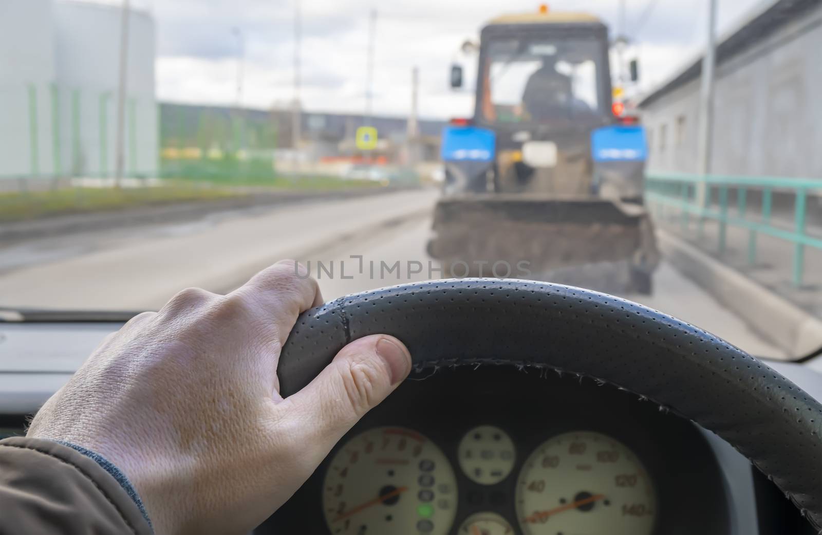 driver hand on the steering wheel of a car that is traveling on the roadway in a jam, makes a maneuver to overtake the tractor