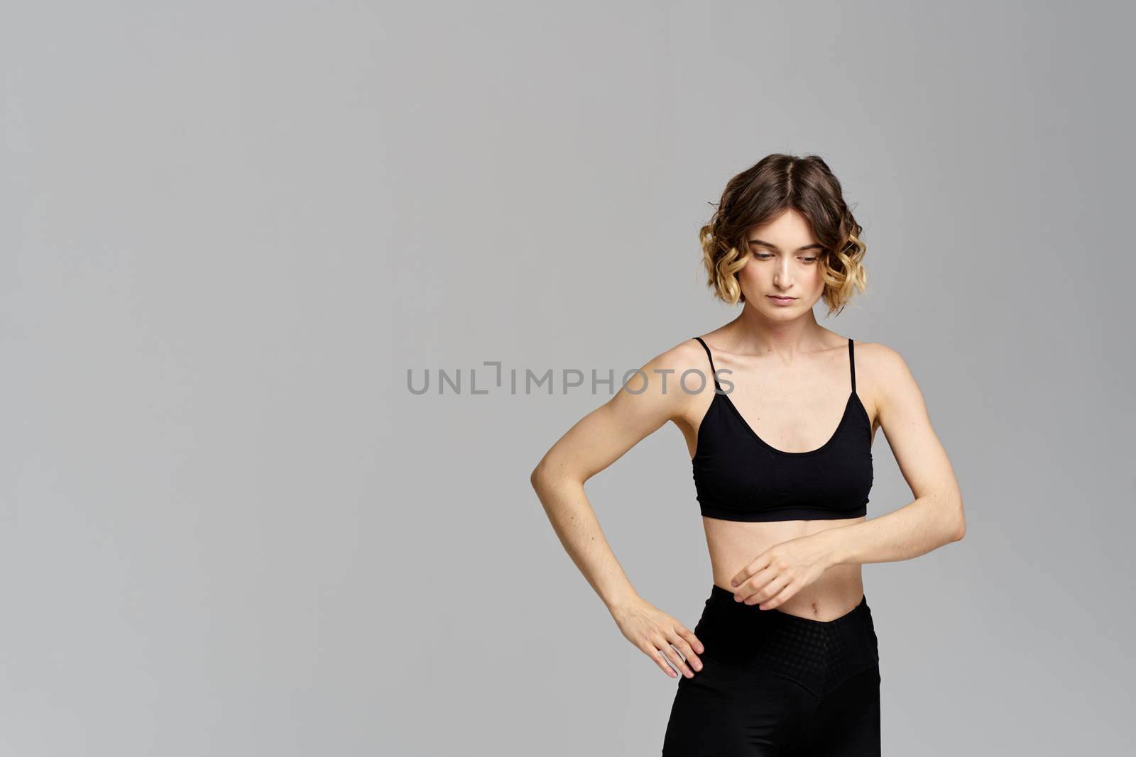 A slender woman in black leggings on a gray background gestures with her hands gymnastics sports. High quality photo