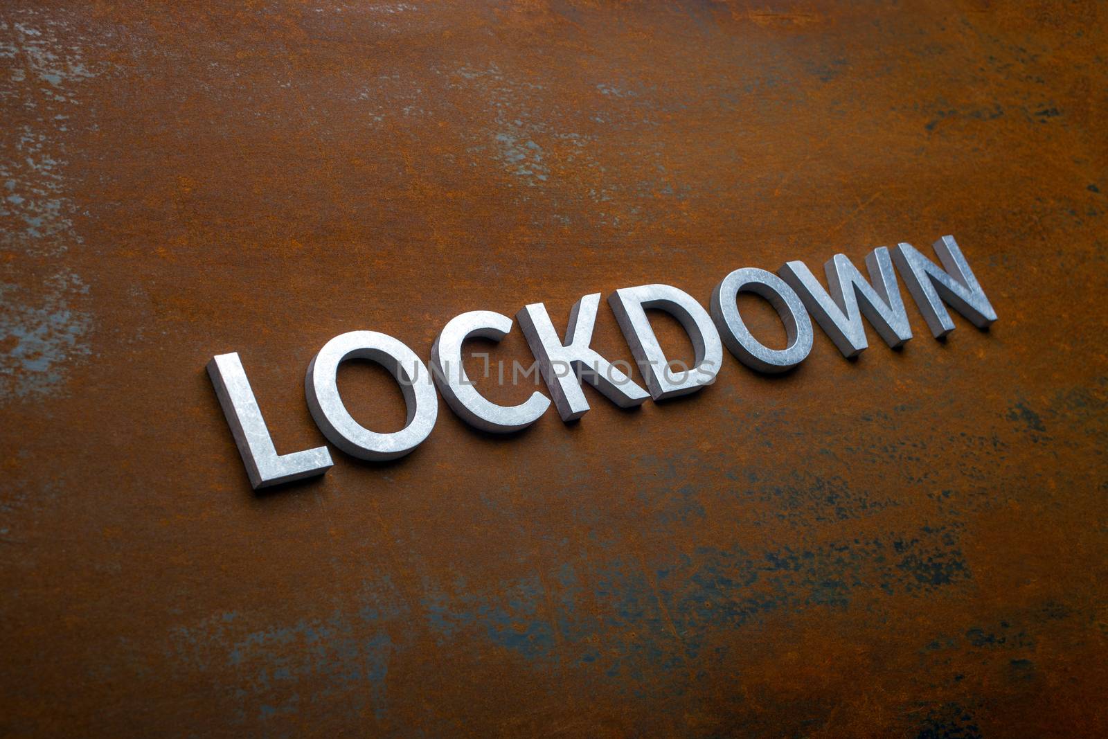 the word lockdown laid with silver metal letters on flat rusted sheet steel background in slanted diagonal perspective with selective focus.