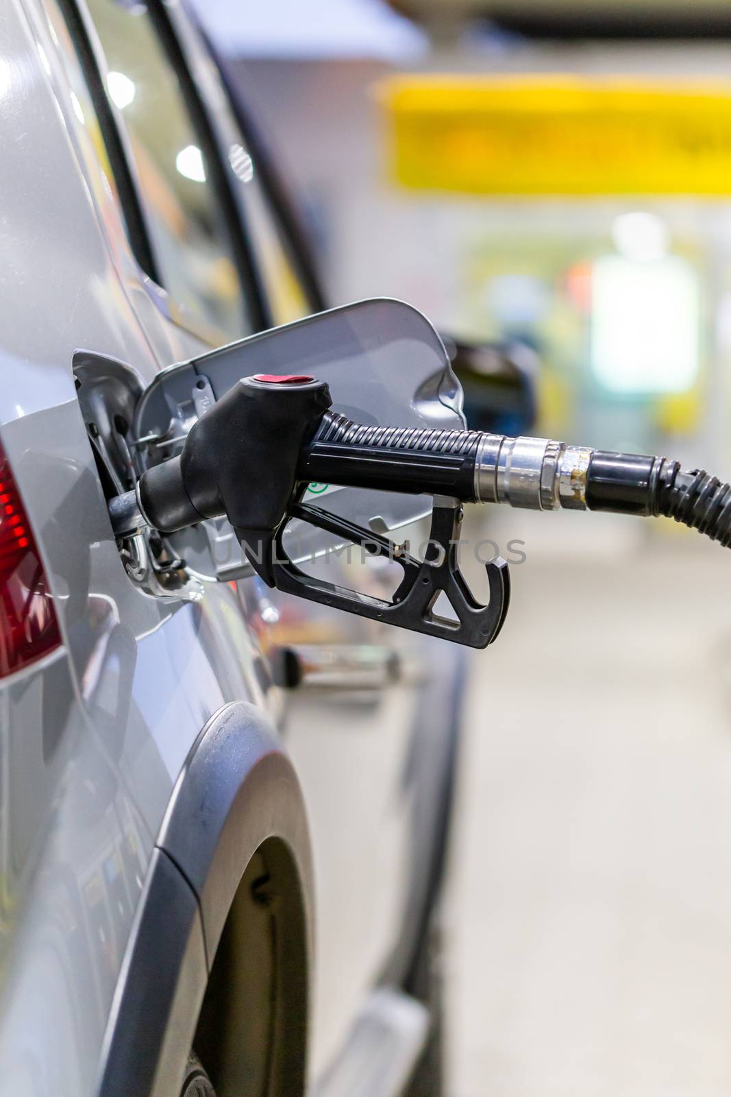 silver mettalic color car refueling on public gas station - close-up with selective focus and blurry background by z1b