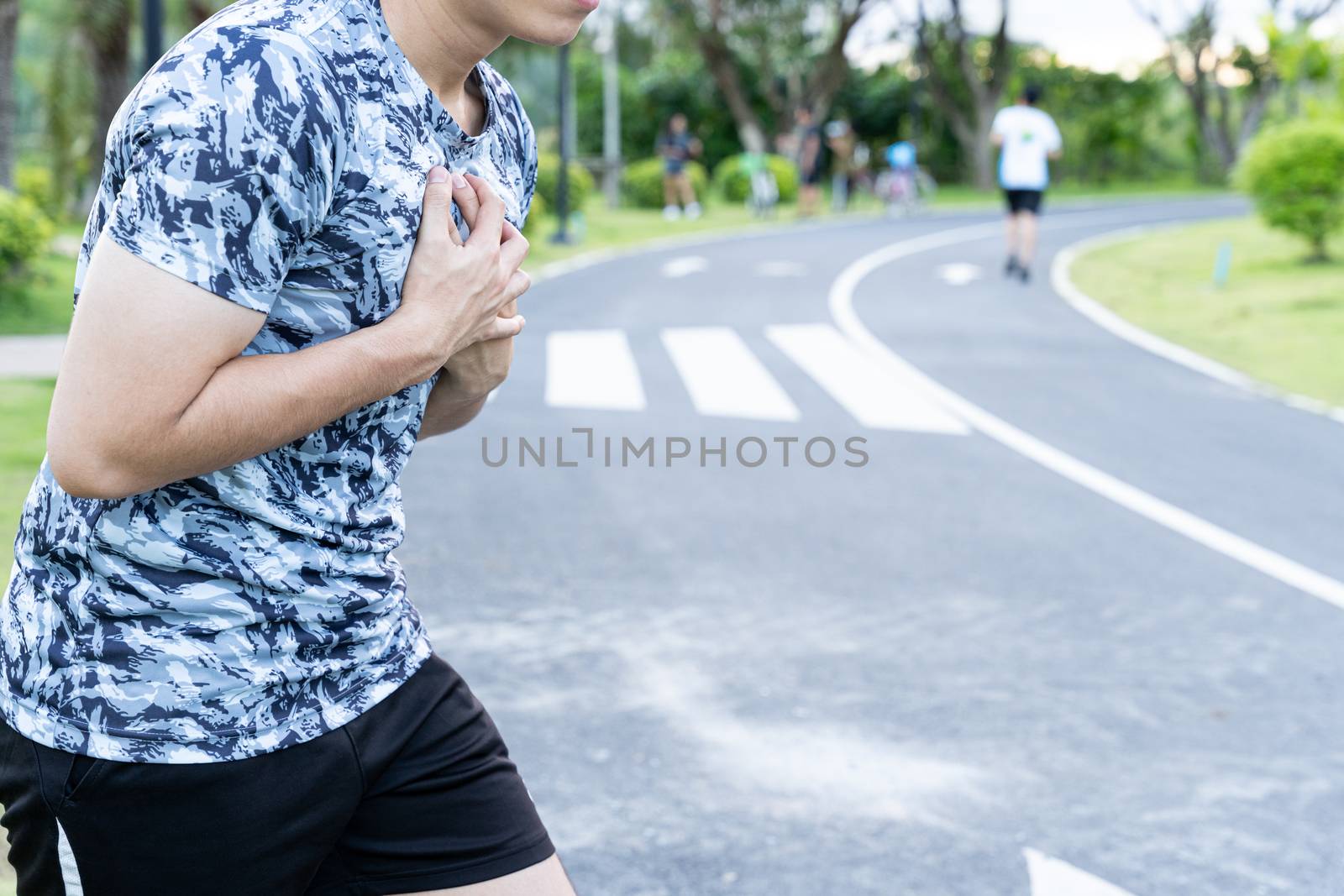 Exhausted male runner suffering painful angina pectoris or asthma breathing problems after running at the park. Sport and healthcare concept.