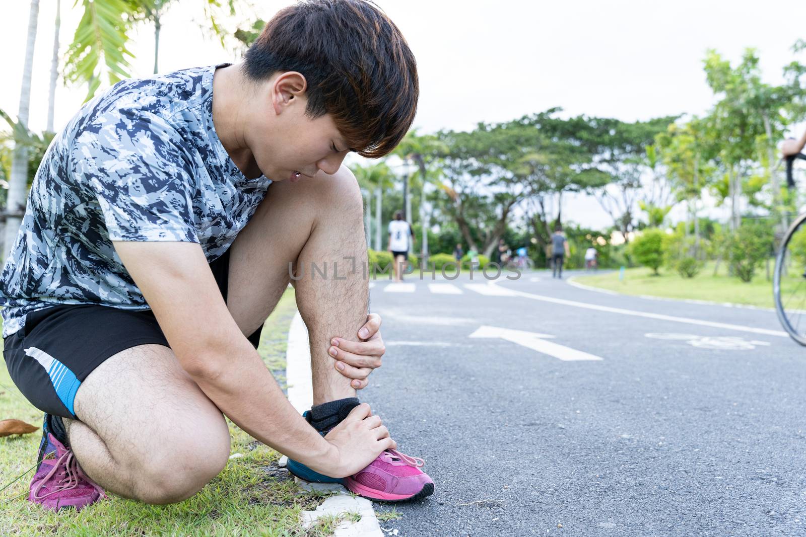 Asian man use hands hold on his ankle while running on road in the park. Injury from workout concept. by mikesaran
