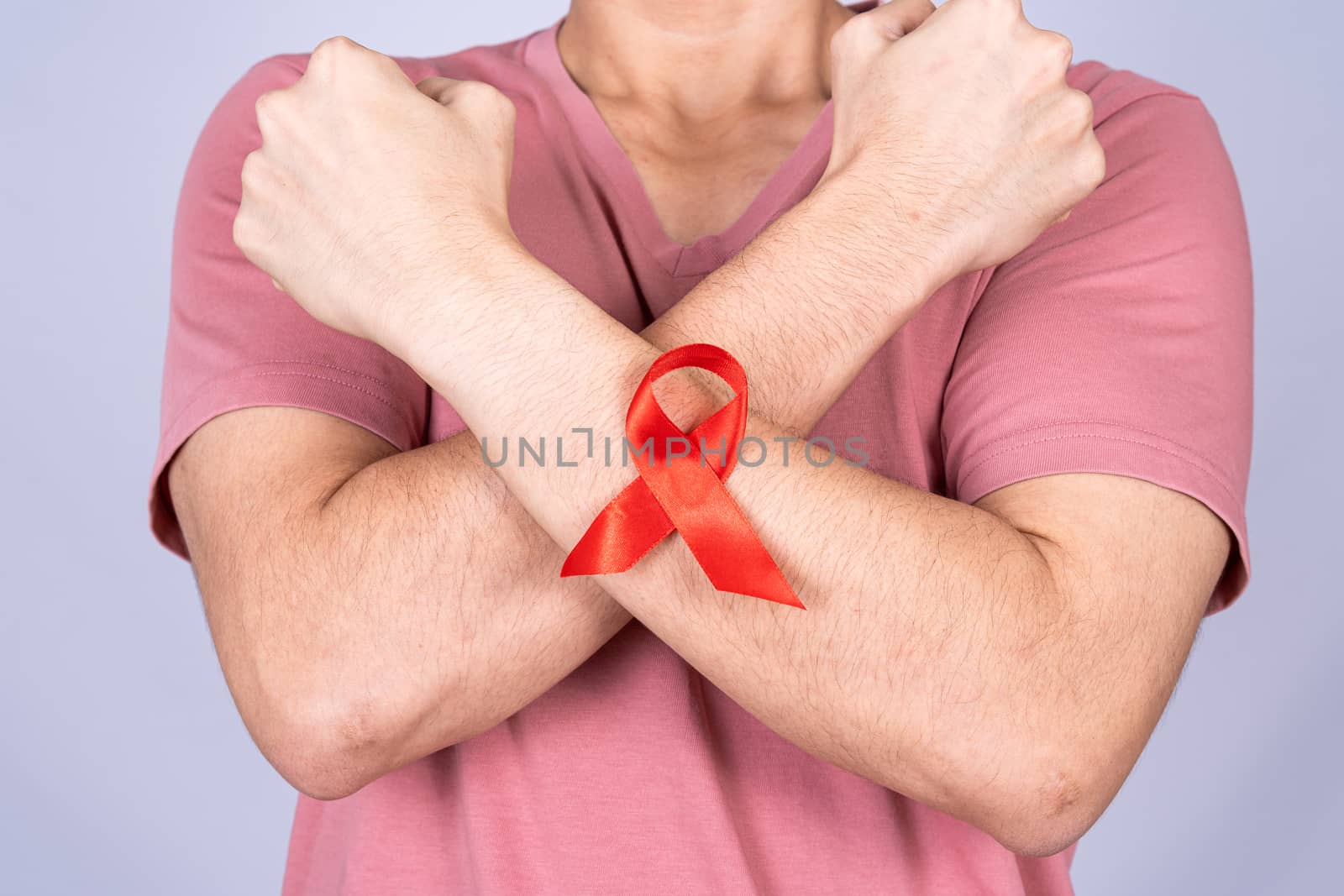 Red AIDS awareness ribbon on man arm and raise his hand to fight them on grey background. World Aids Day, Healthcare and medical concept.