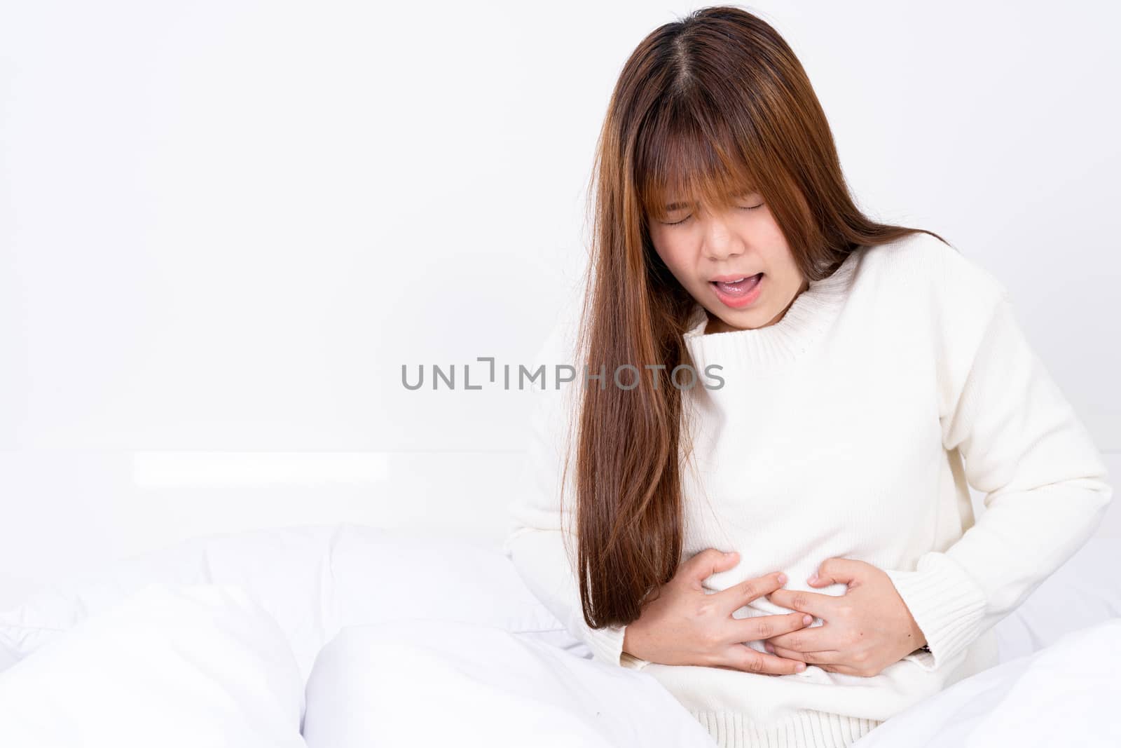 Young woman suffering stomach aches lying on the bed. Healthcare medical or daily life concept. by mikesaran