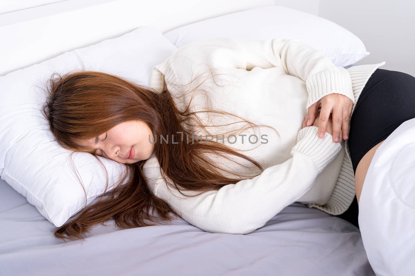 Young woman suffering stomach aches lying on the bed. Healthcare medical or daily life concept. by mikesaran