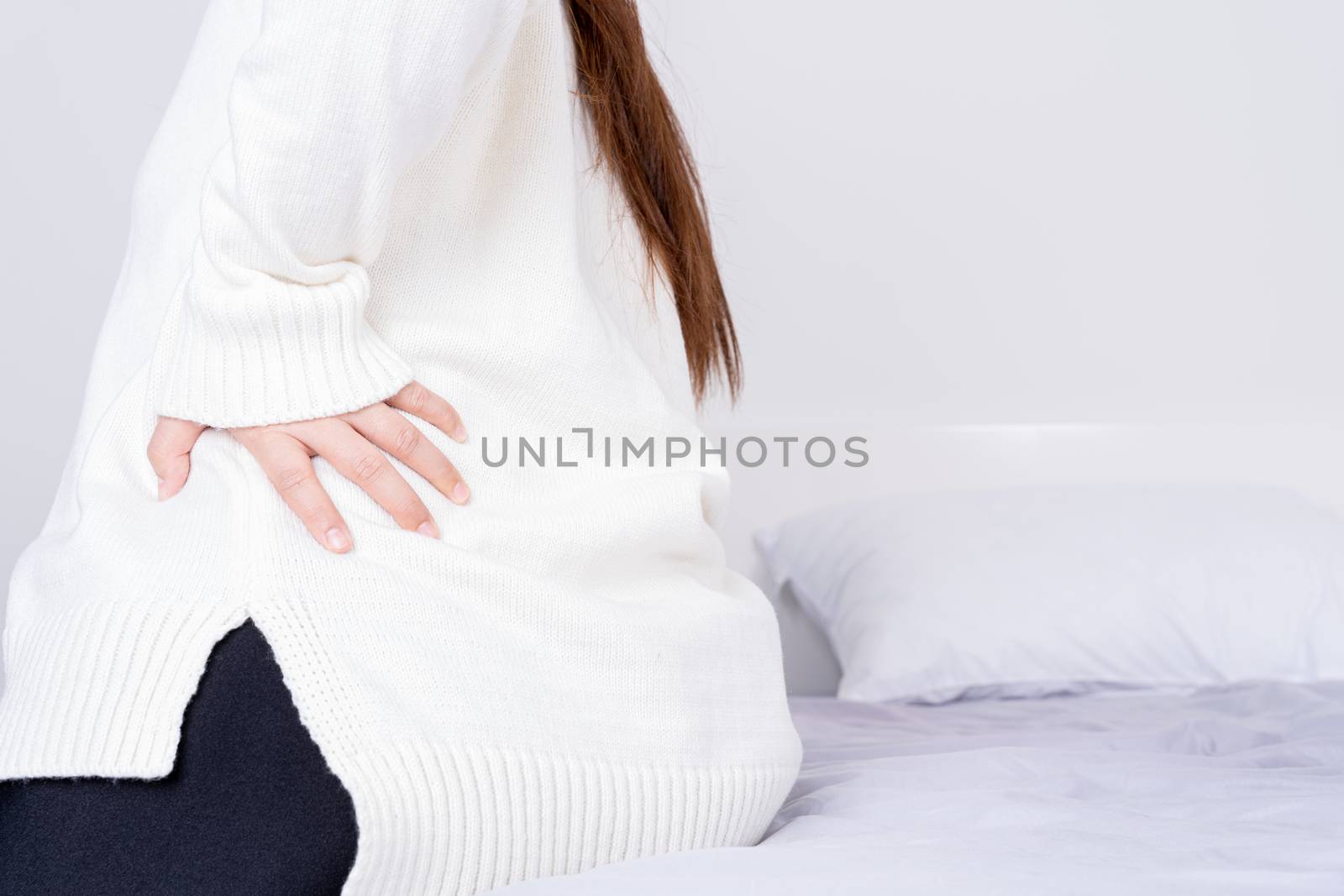 Young woman suffering back pain from uncomfortable bed. Healthcare medical or daily life concept.