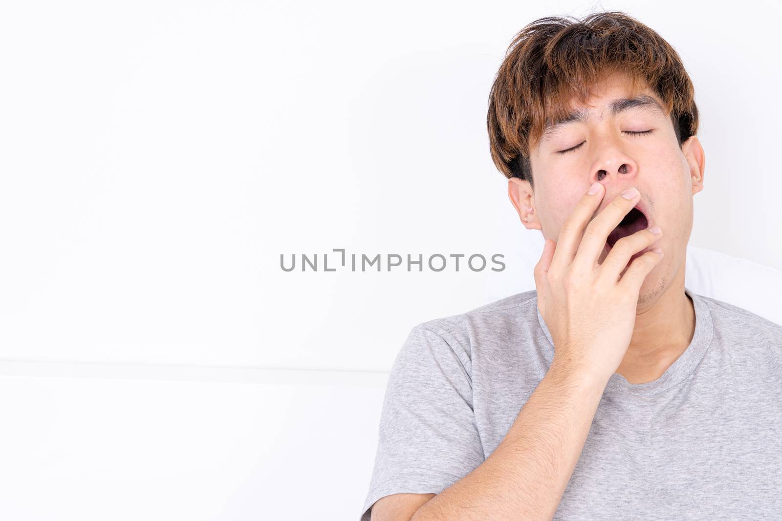 Asian man are yawning covering open mouth with hand after he wake up. Healthcare medical or daily life concept. by mikesaran