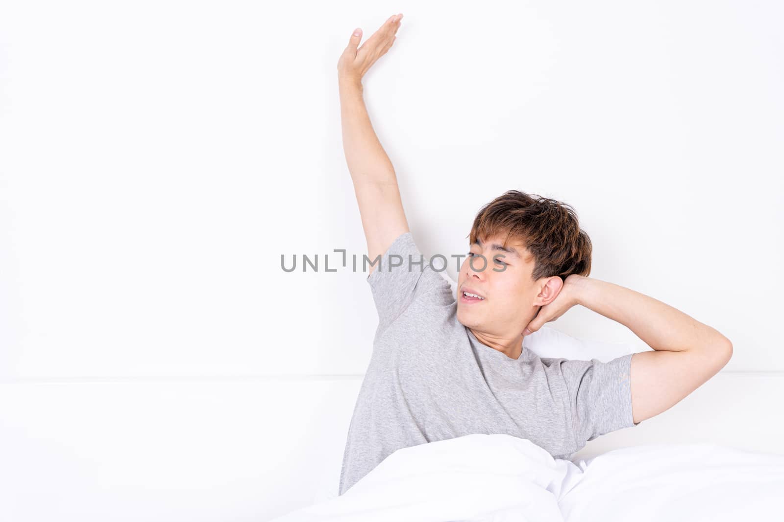 Young Asian man stretching in bed after wake up from the good comfortable bed. Healthcare medical or daily life concept. by mikesaran