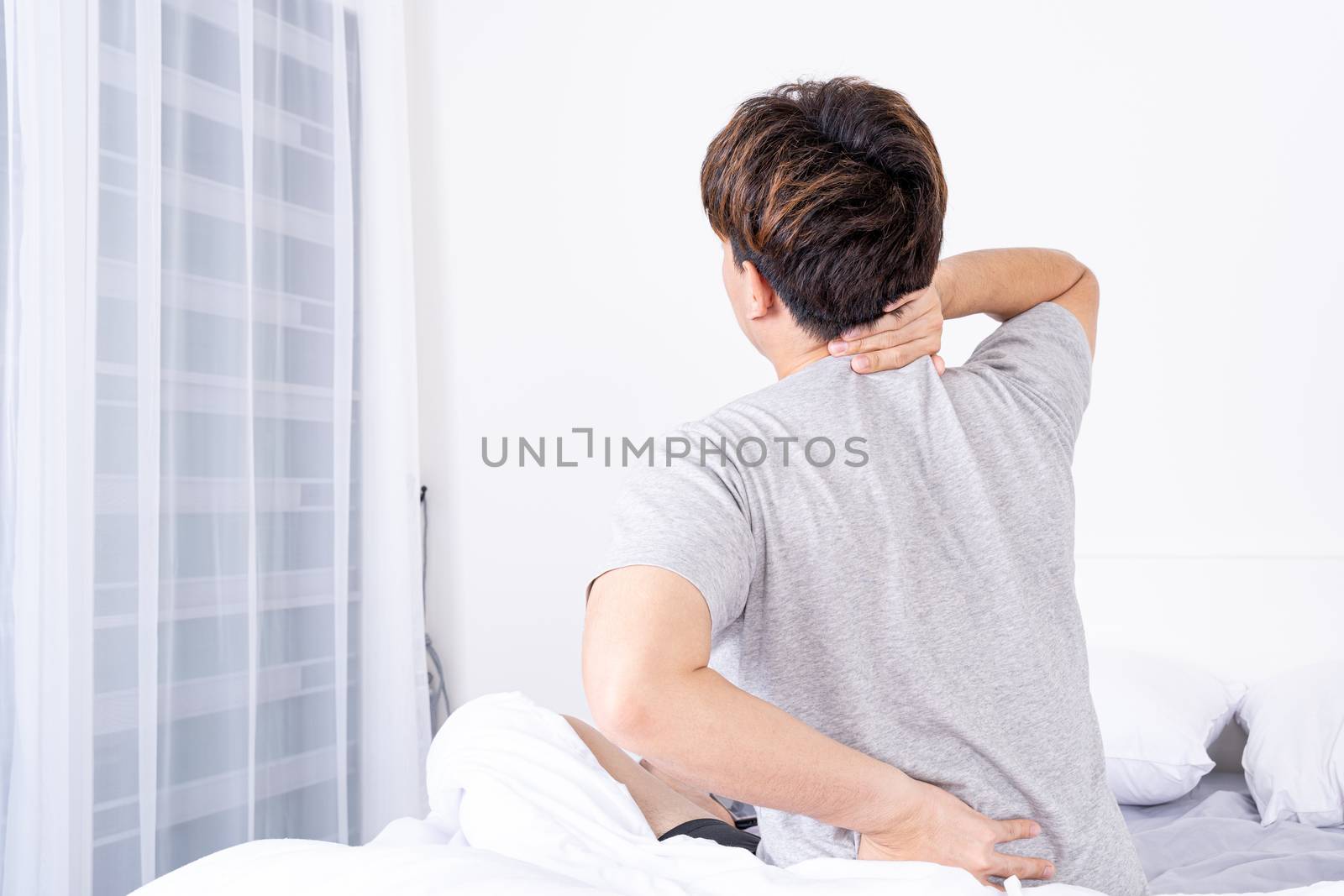 Young man suffering neck and back pain from uncomfortable bed. Healthcare medical or daily life concept.