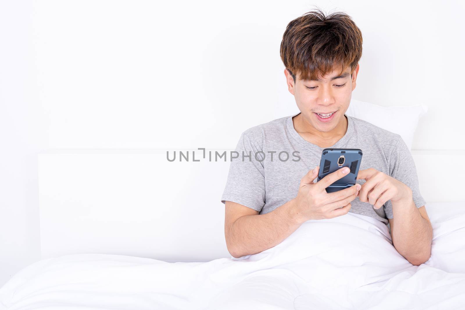 Happy Asian man using a mobile phone lying on the bed at home. Social and technology concept.