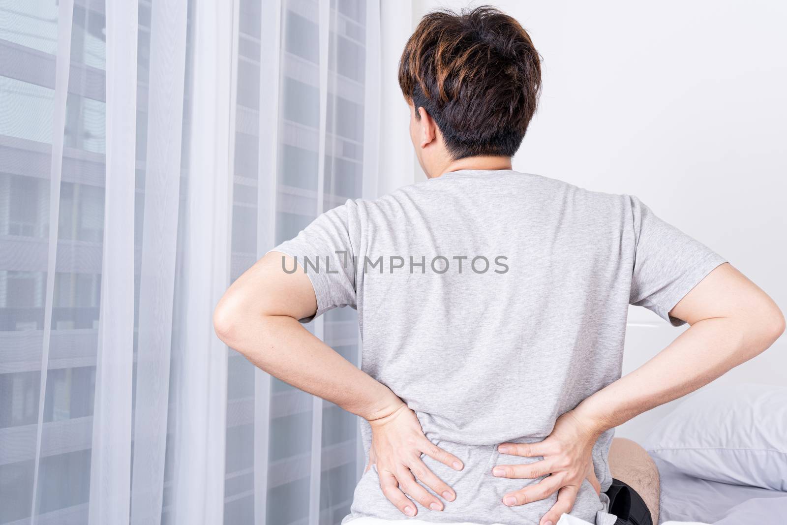 Young man suffering back pain from uncomfortable bed. Healthcare medical or daily life concept.