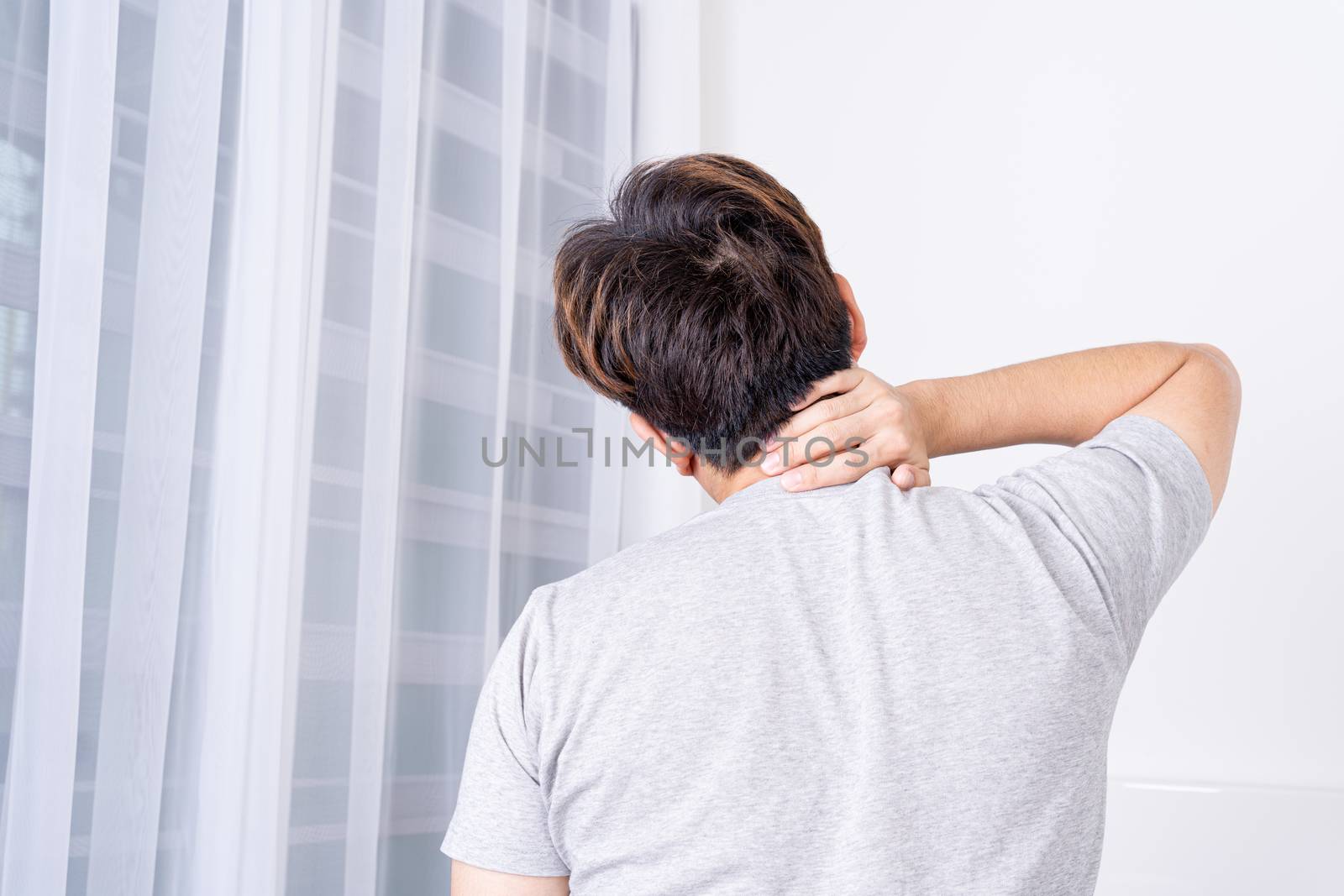 Young man suffering neck and shoulder pain from uncomfortable bed. Healthcare medical or daily life concept.