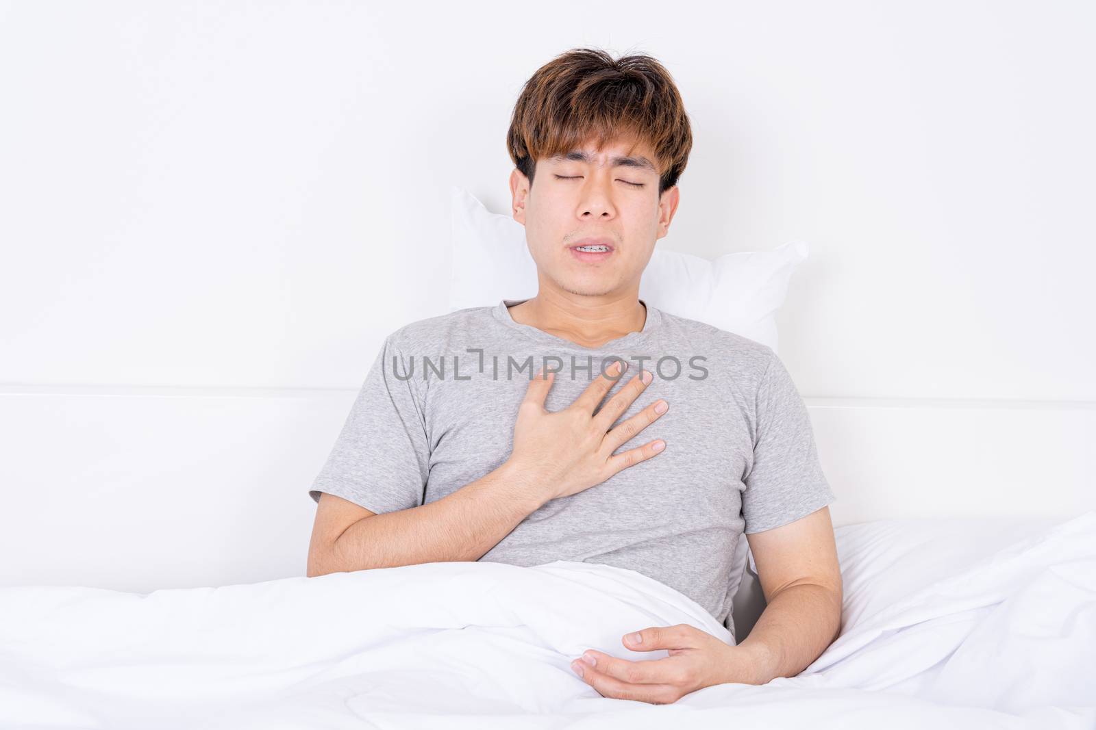 Young man suffering from chest pain after wake up on the bed. Healthcare medical or daily life concept.