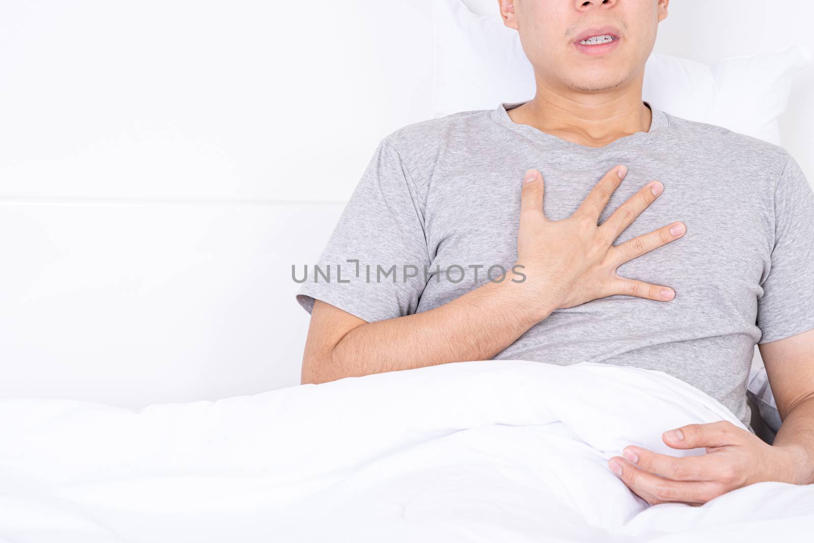 Young man suffering from chest pain after wake up on the bed. Healthcare medical or daily life concept. by mikesaran