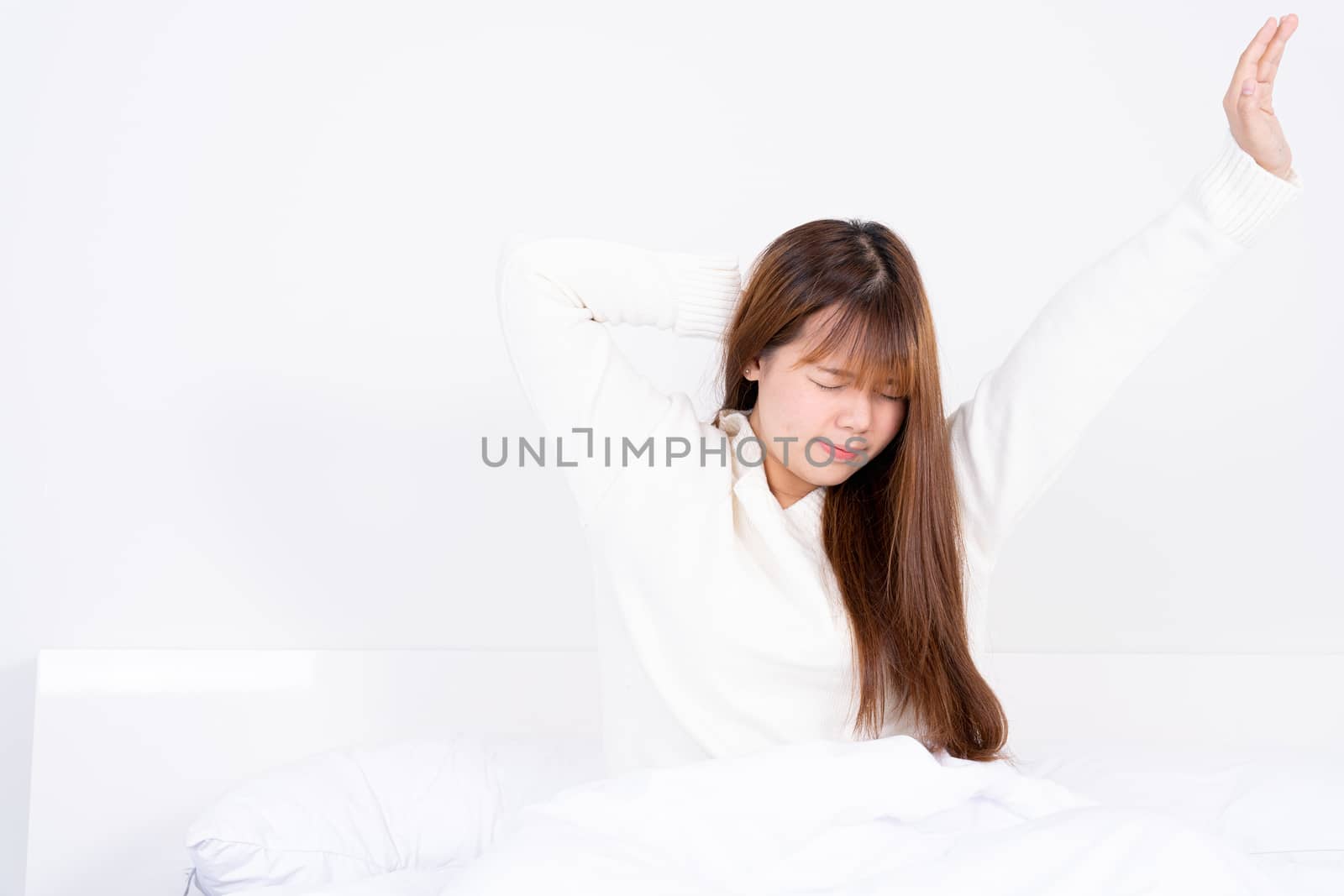 Young Asian woman stretching in bed after wake up from the good comfortable bed. Healthcare medical or daily life concept.