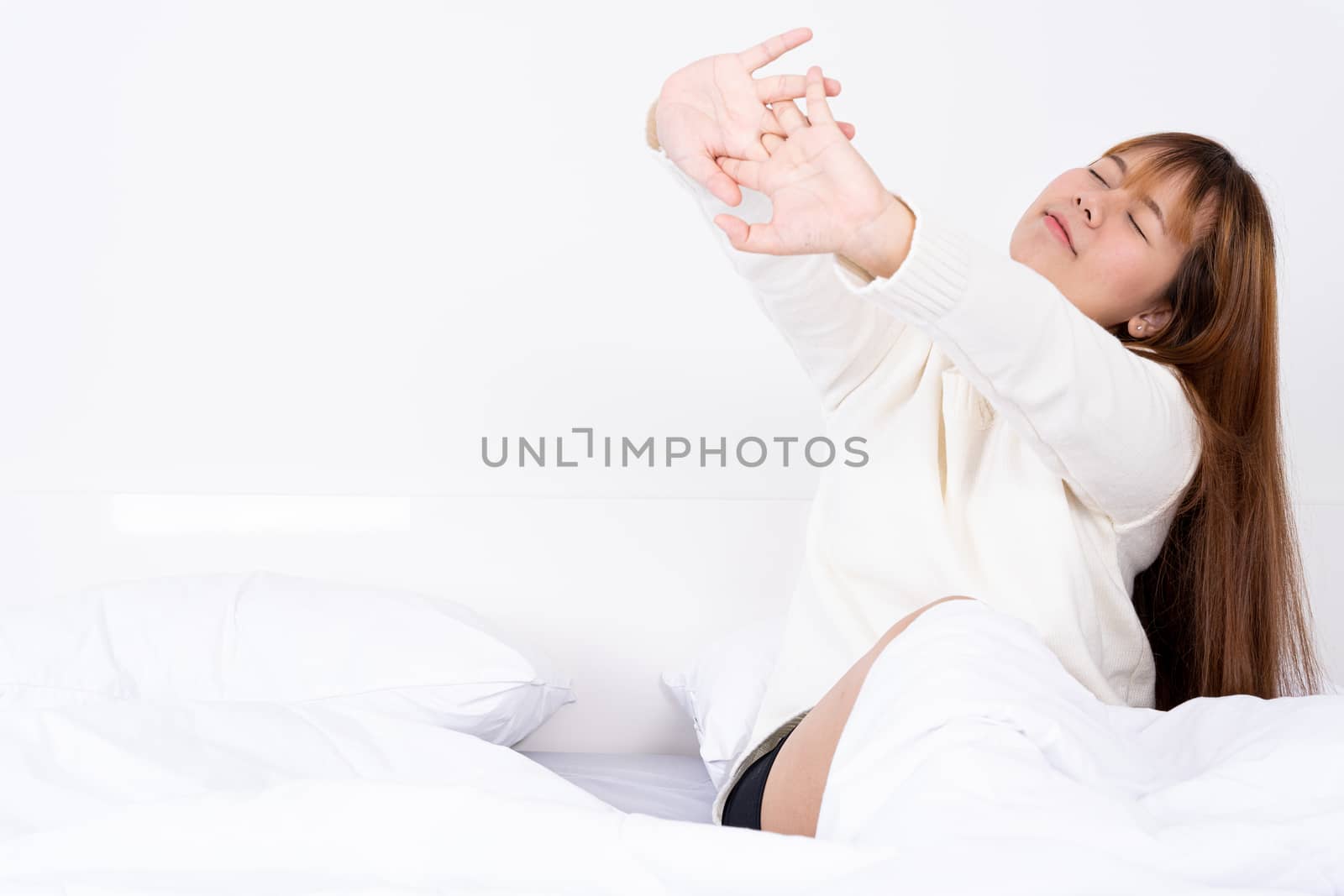 Young Asian woman stretching in bed after wake up from the good comfortable bed. Healthcare medical or daily life concept.