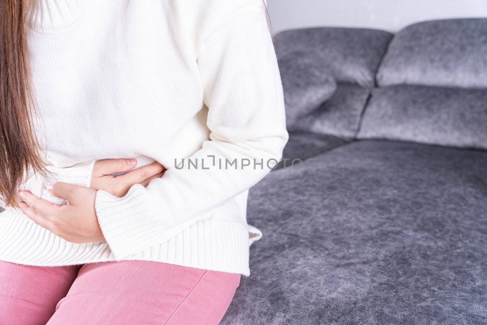 Young woman suffering from strong abdominal pain or menstruation while sitting on sofa at home. Healthcare medical or daily life concept. by mikesaran