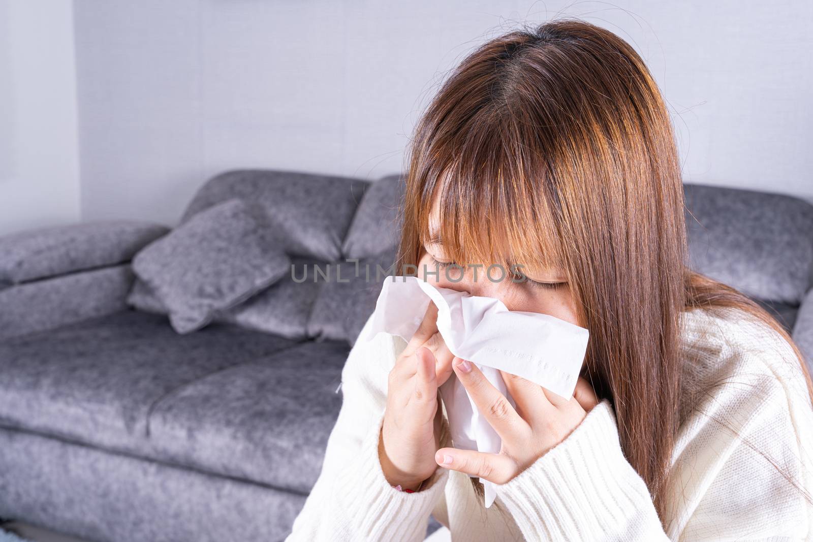 Asian beautiful woman blowing a nose to tissue while sitting on sofa at home. Healthcare medical or daily life concept.