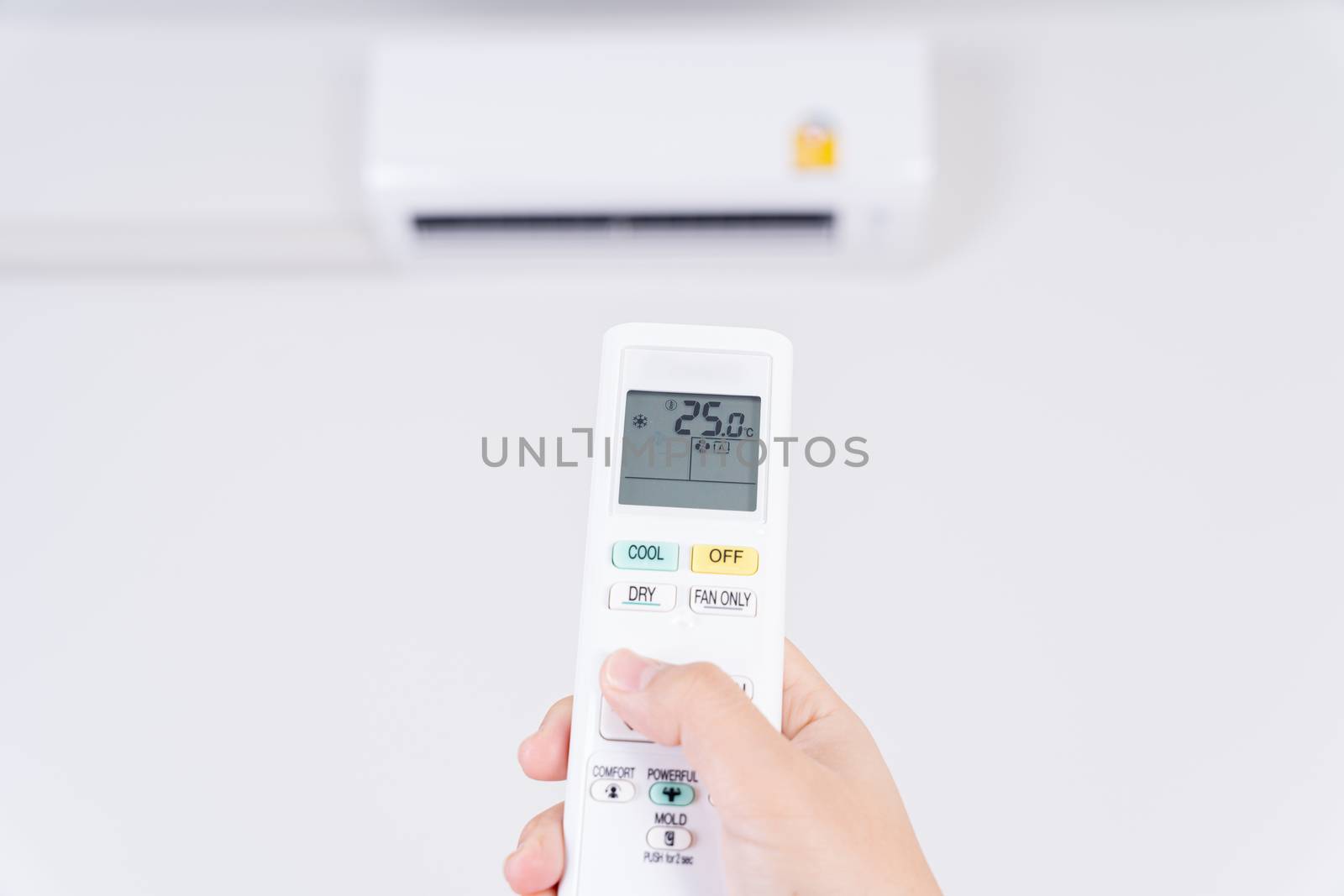 Human hand is using white remote of air conditioner for turn on or adjust temperature of air conditioner inside the room.