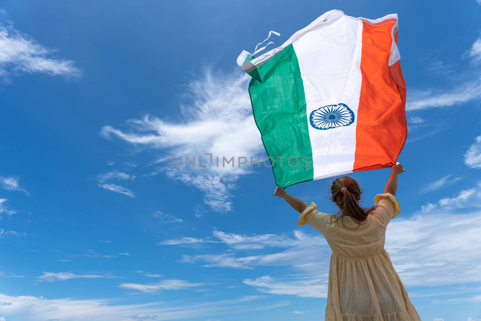 woman standing and holding India flag under blue sky. by mikesaran