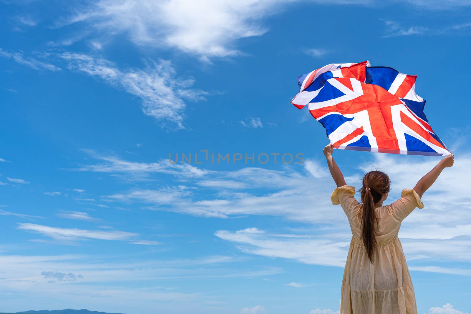 woman standing and holding UK flag under blue sky. by mikesaran