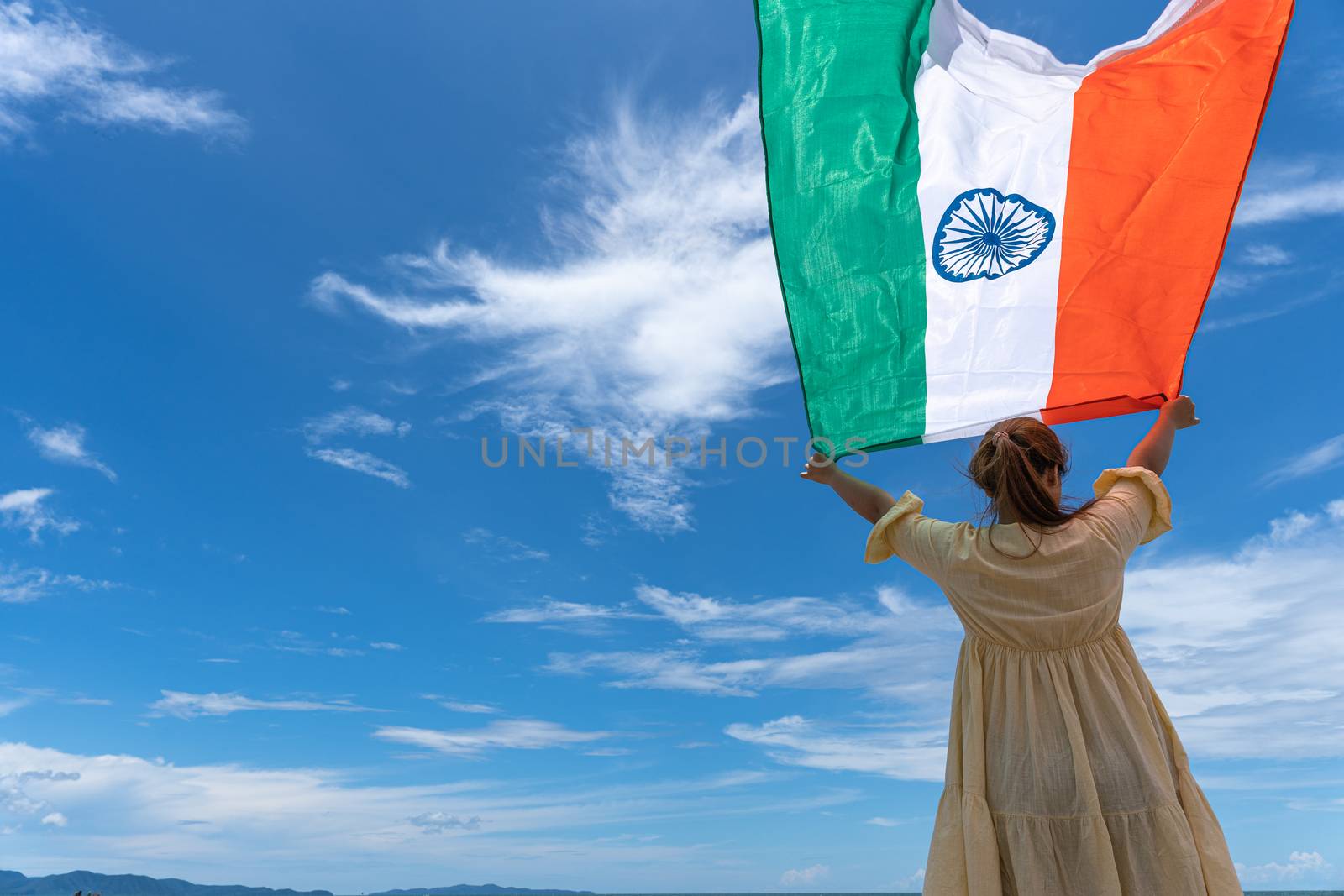 woman standing and holding India flag under blue sky.