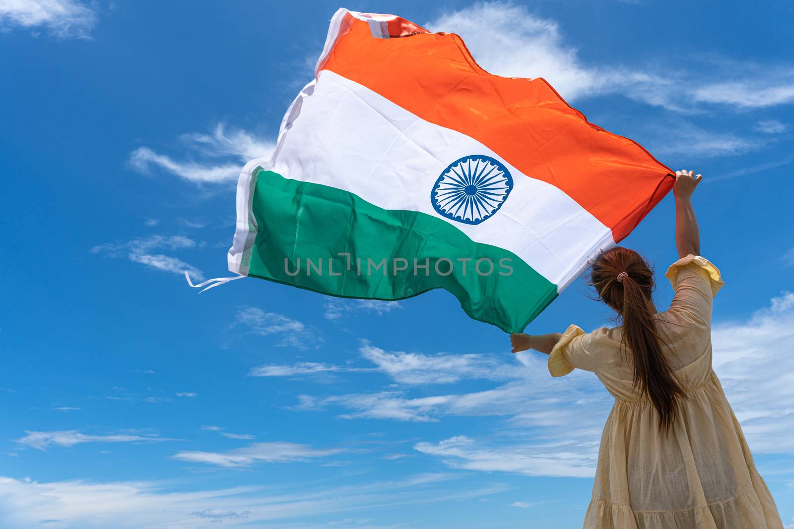 woman standing and holding India flag under blue sky. by mikesaran