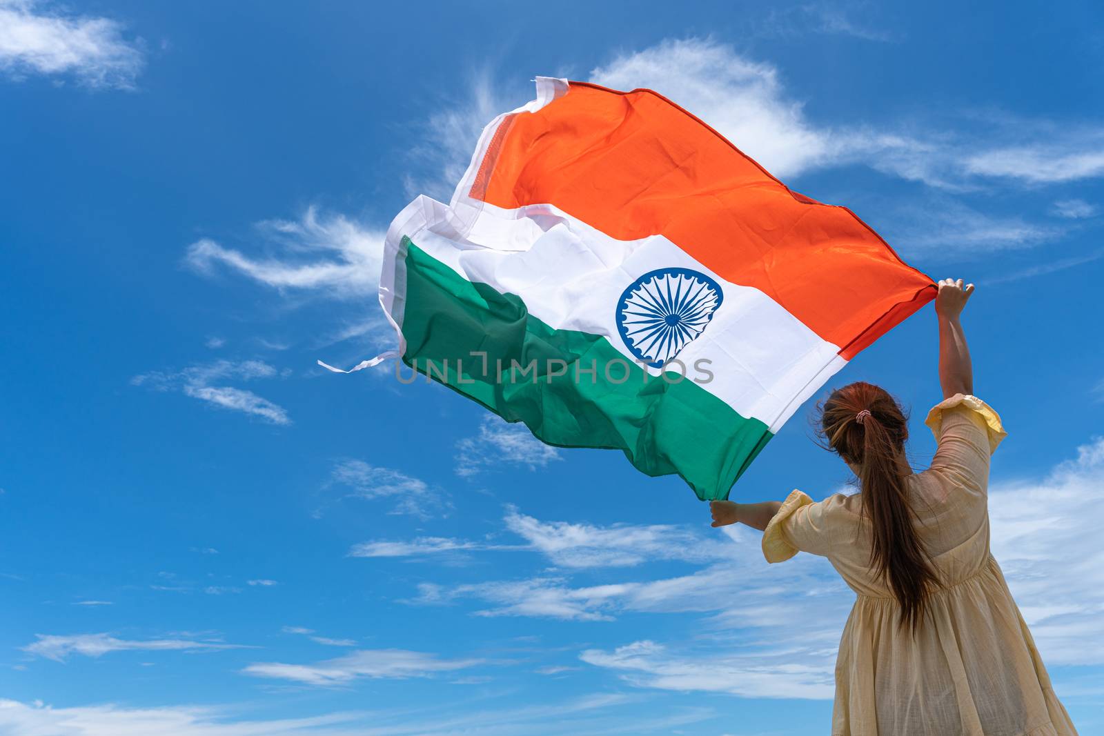 woman standing and holding India flag under blue sky. by mikesaran