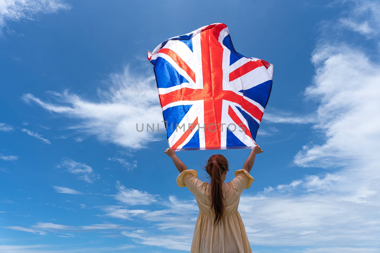 woman standing and holding UK flag under blue sky.