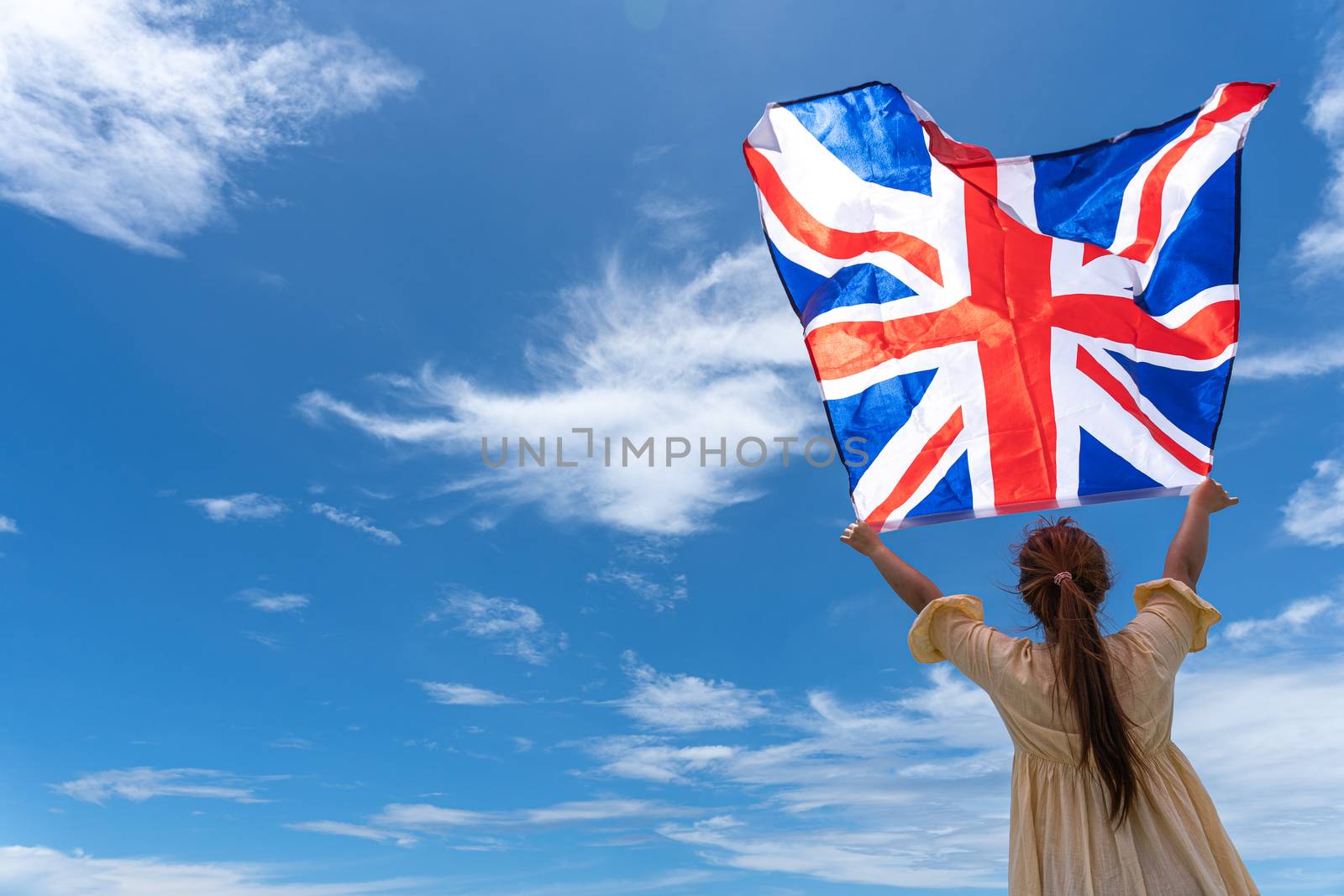 woman standing and holding UK flag under blue sky.