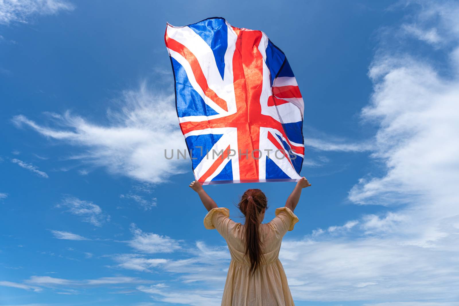 woman standing and holding UK flag under blue sky. by mikesaran