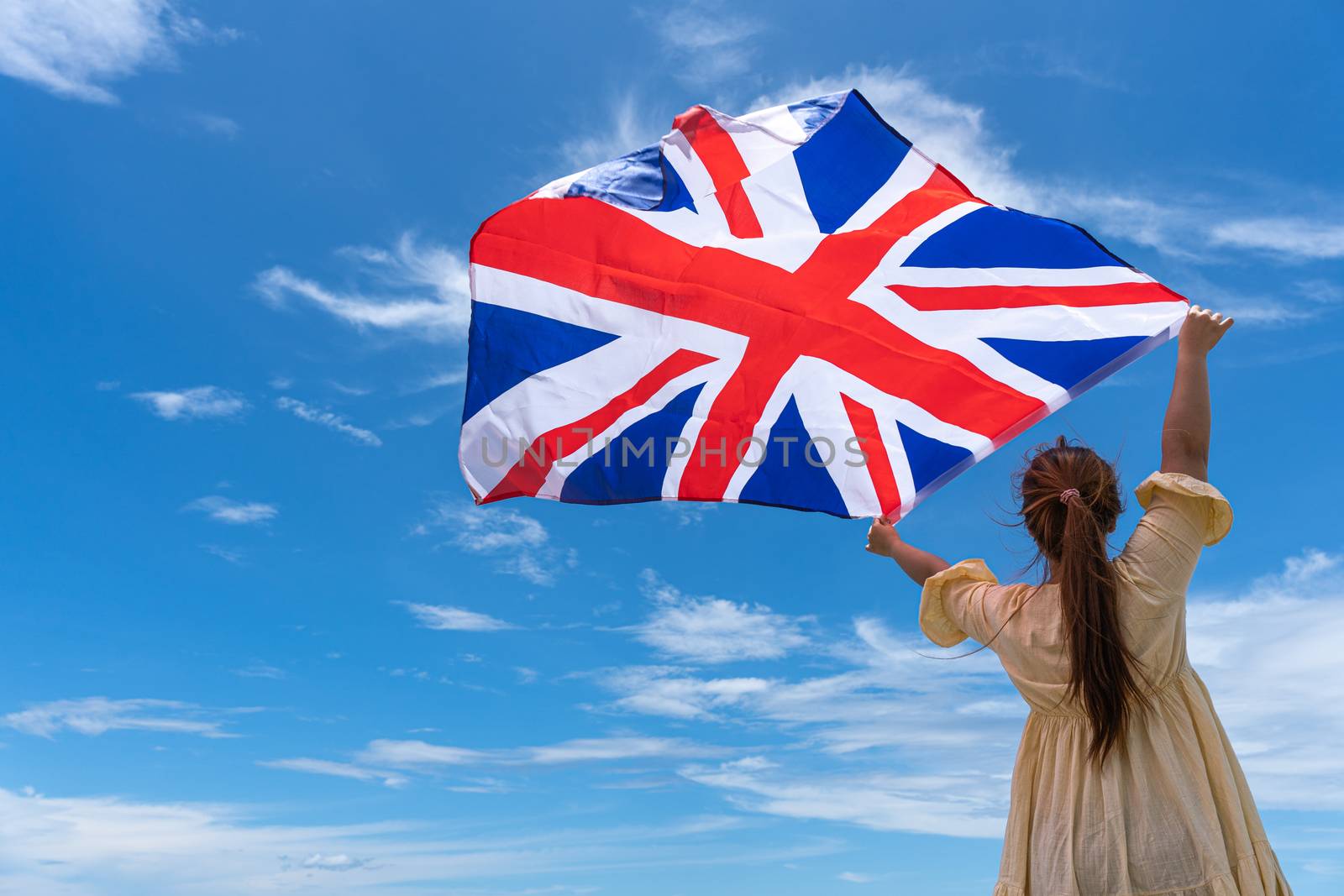 woman standing and holding UK flag under blue sky. by mikesaran