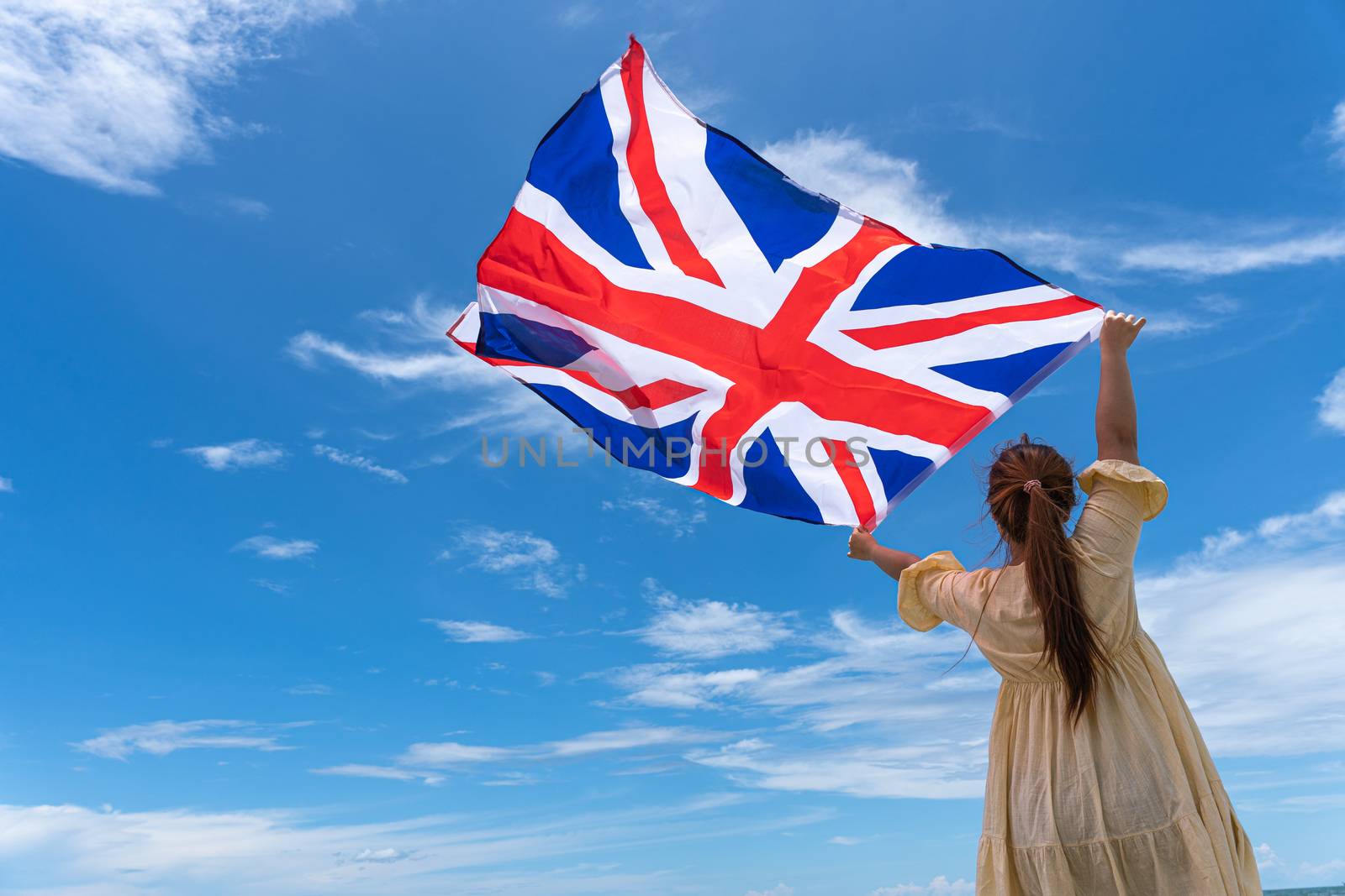 woman standing and holding UK flag under blue sky.