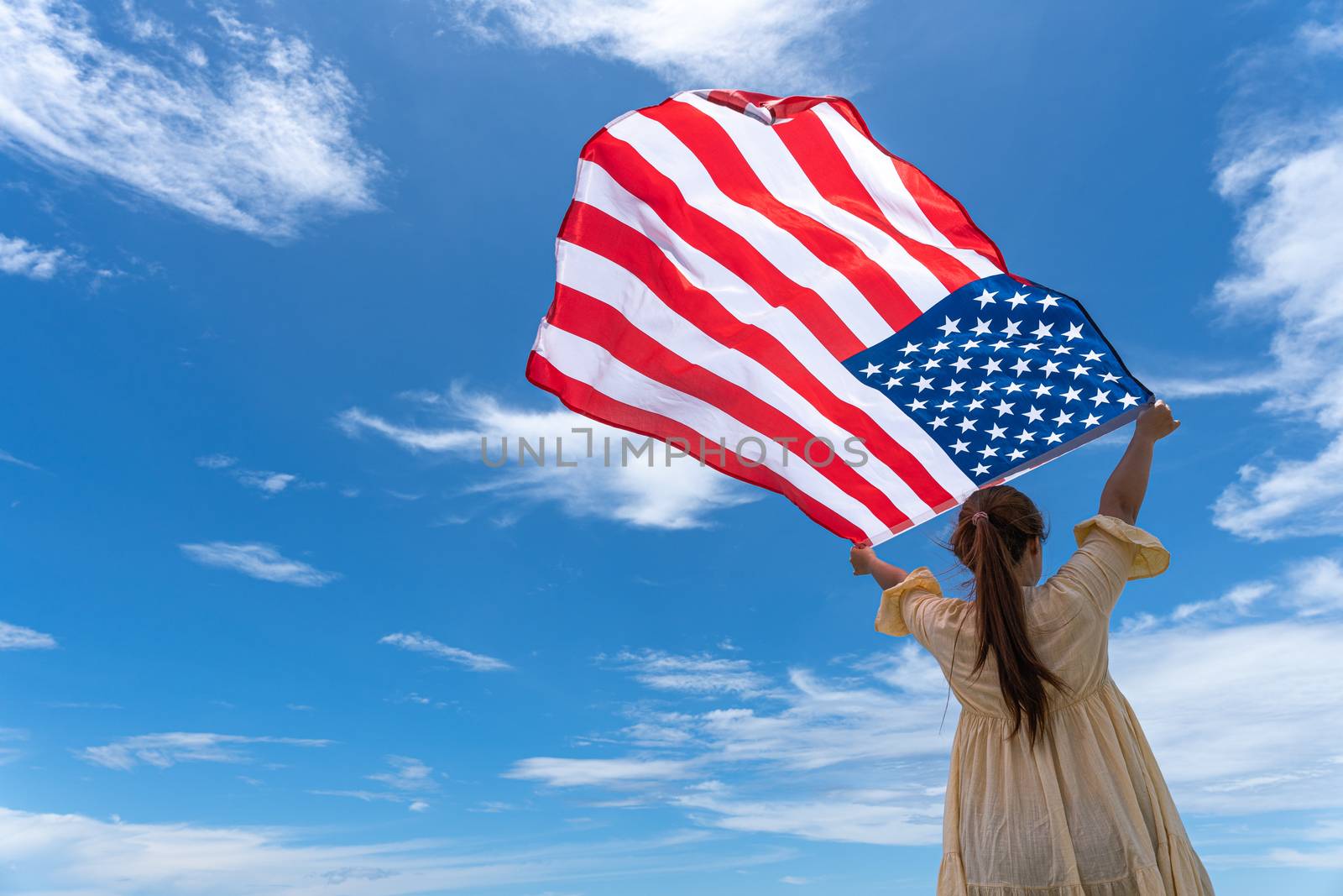 woman standing and holding USA flag under blue sky.