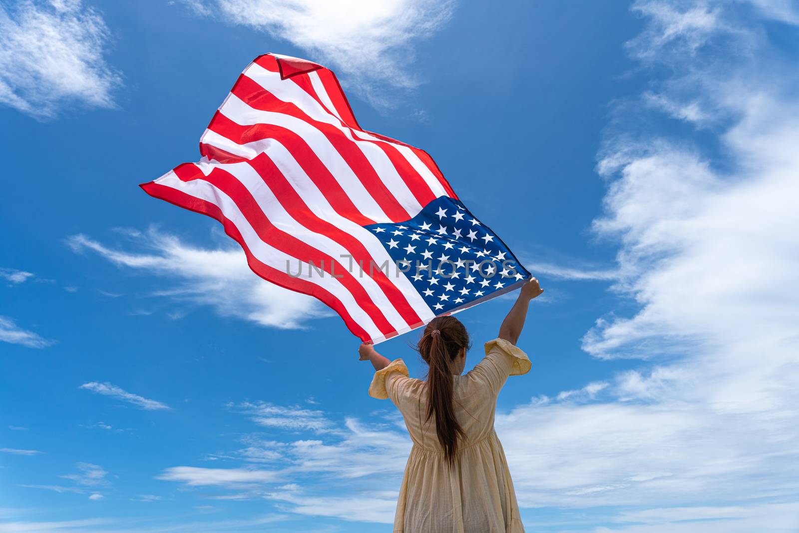 woman standing and holding USA flag under blue sky. by mikesaran