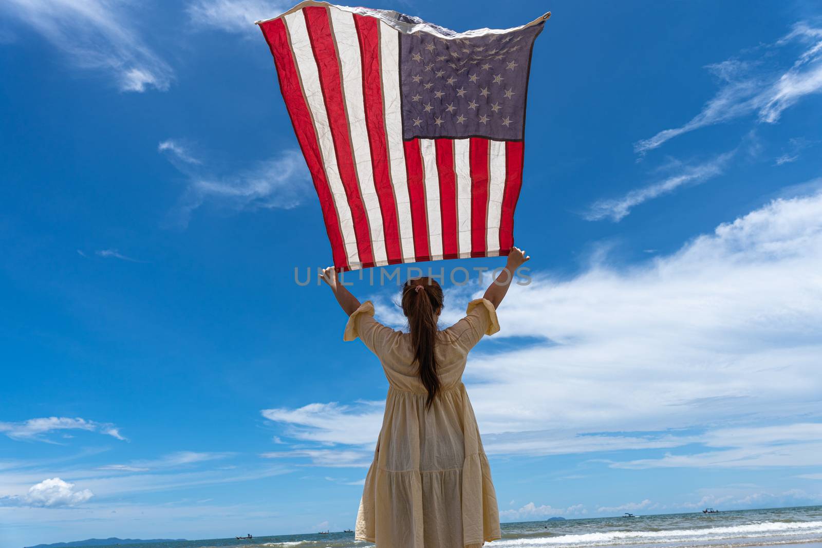 woman standing and holding USA flag under blue sky.