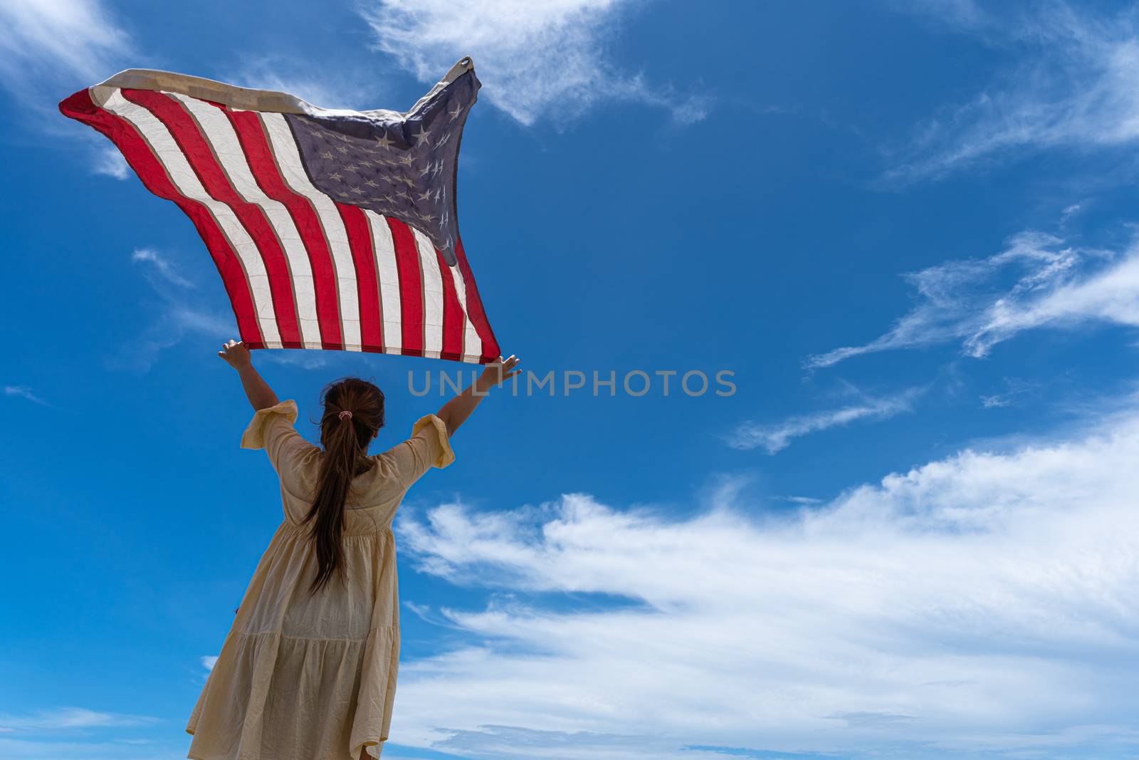 woman standing and holding USA flag under blue sky.