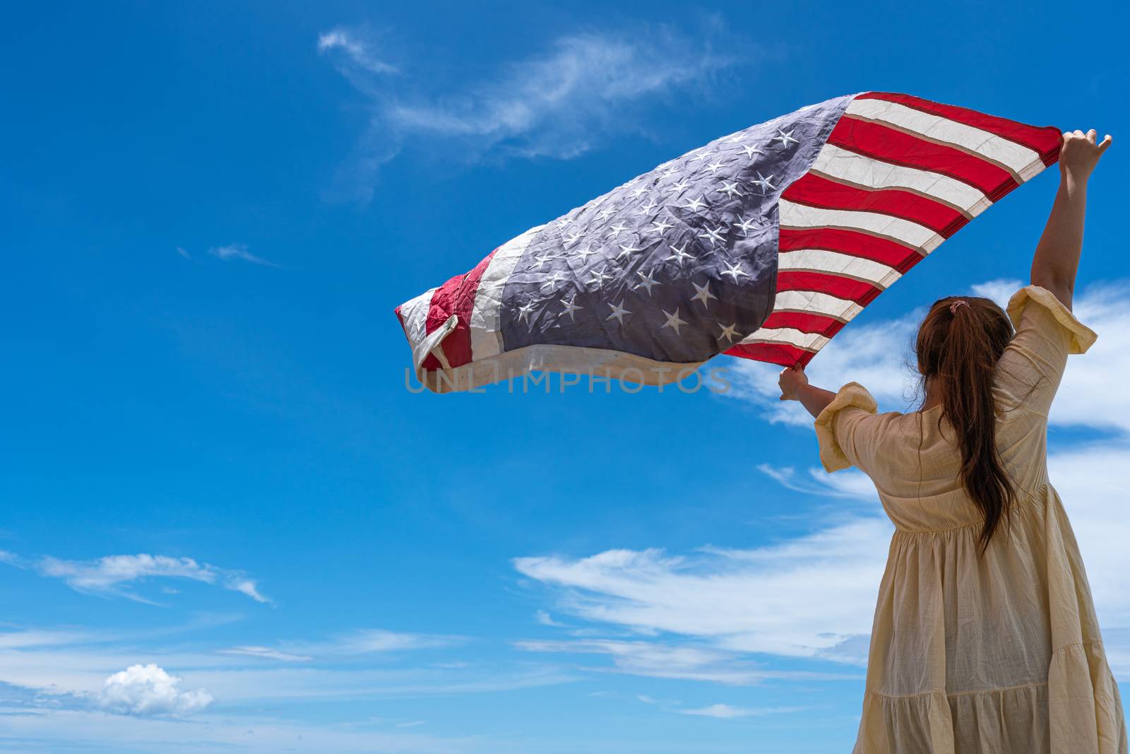 woman standing and holding USA flag under blue sky. by mikesaran