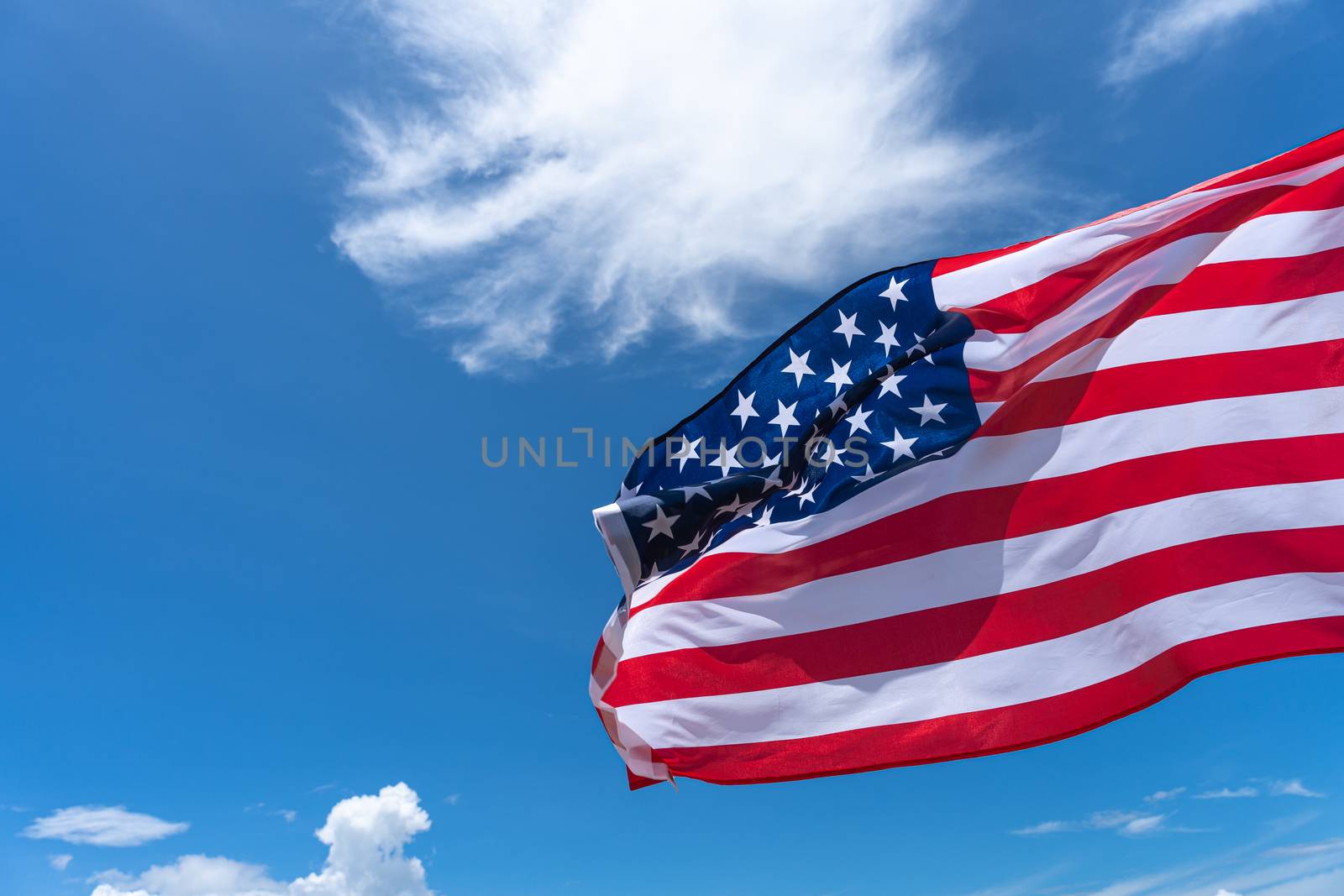 Waving USA flag under blue sky background.