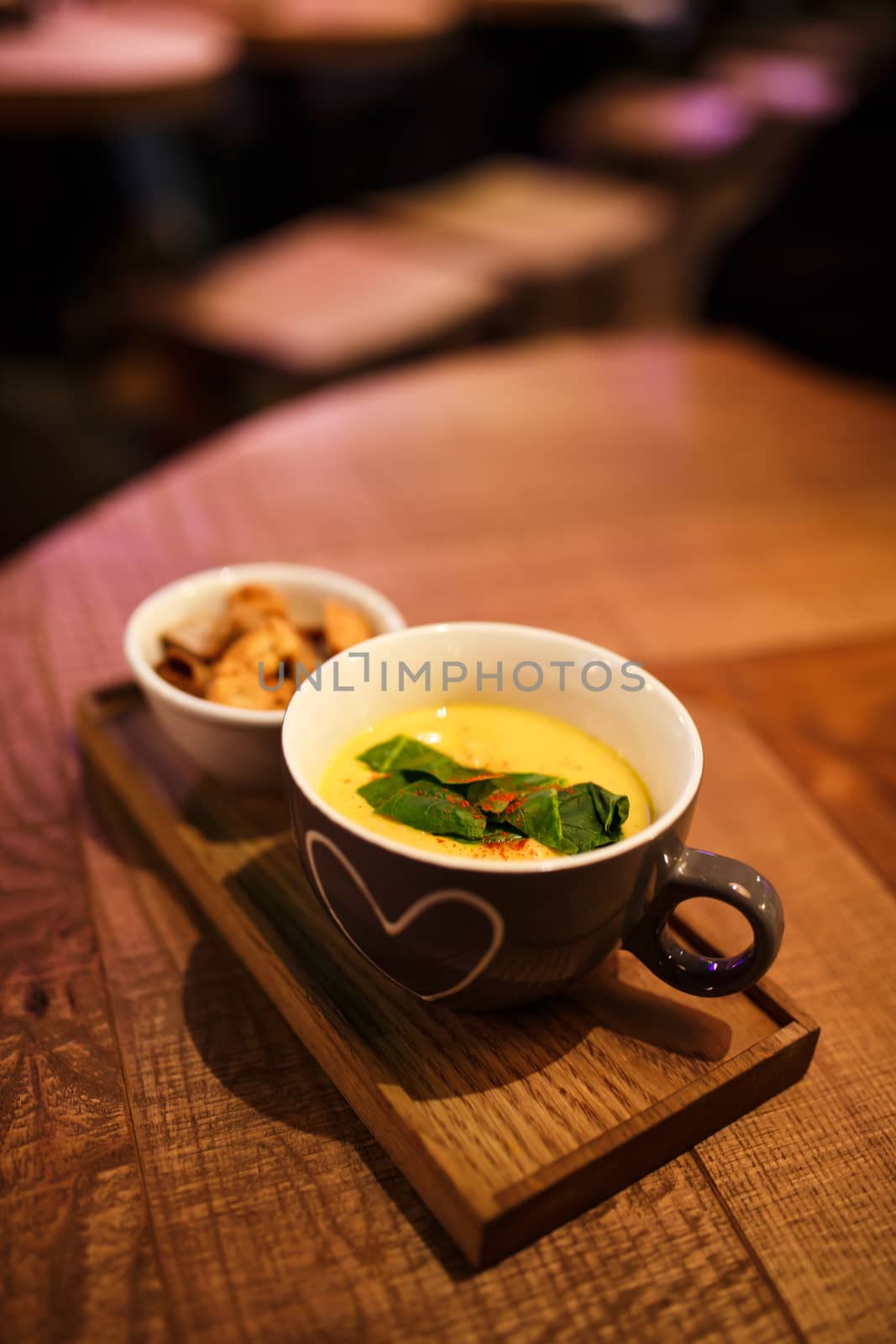 Serving cream soup in a cup with a cup of rusks on a wooden tray.