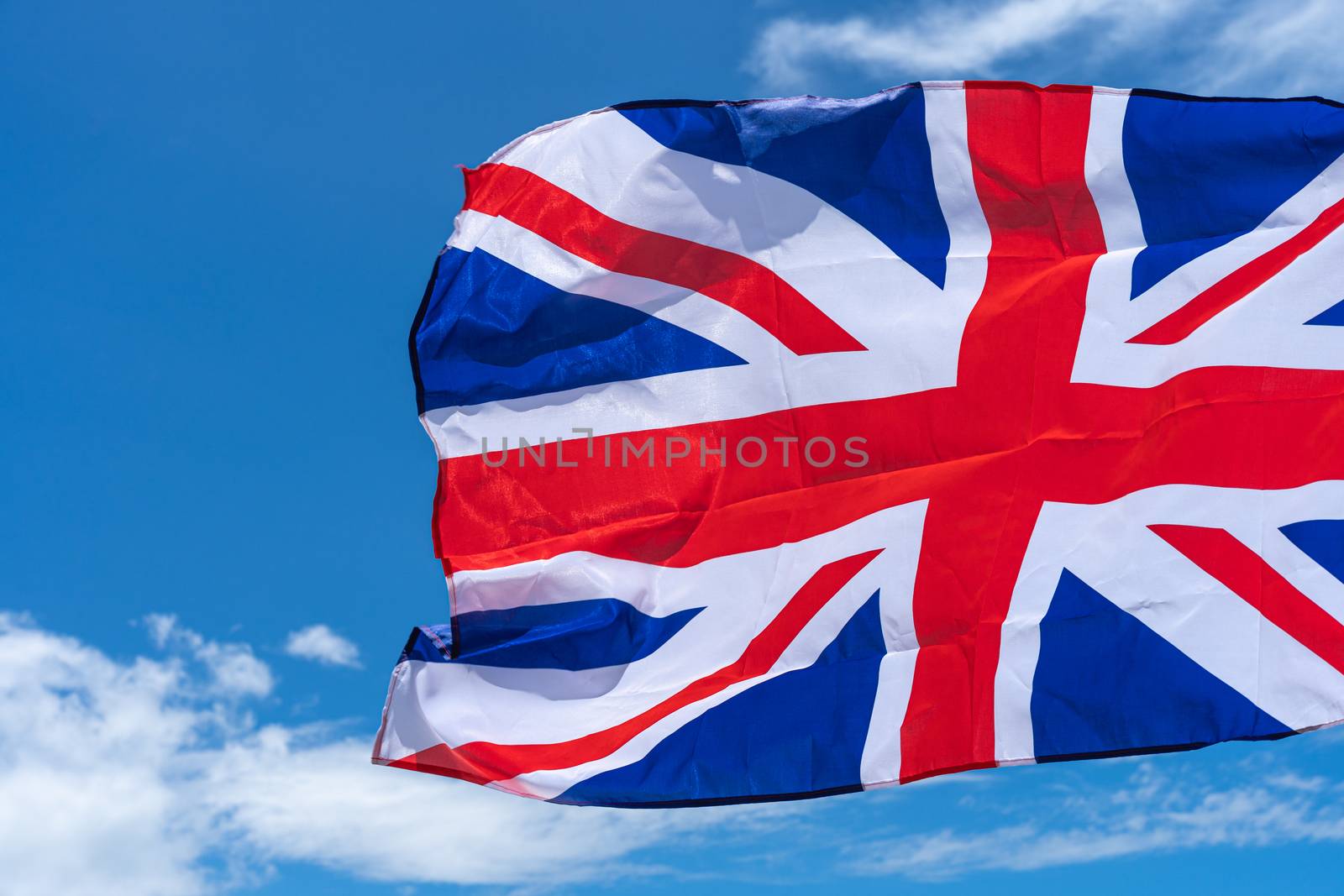Waving UK flag under blue sky background.