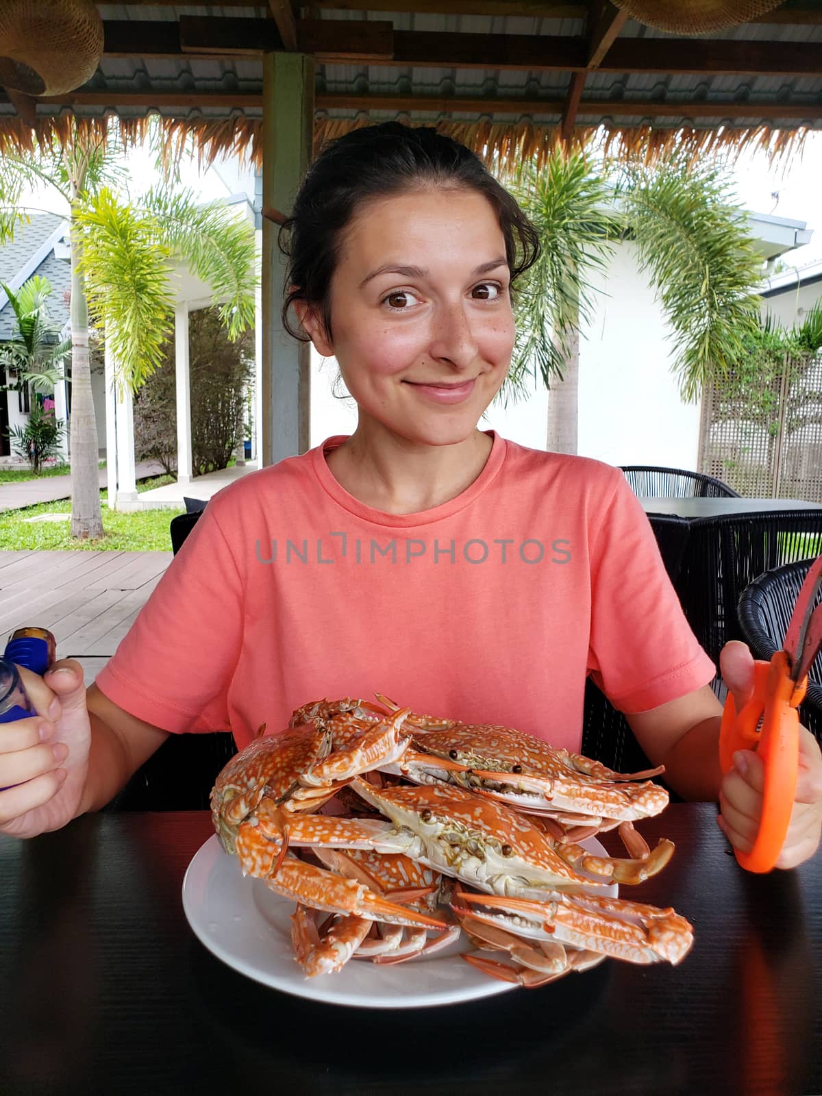 The girl is going to eat boiled crabs. The girl at the table with a full plate of boiled blue crabs.