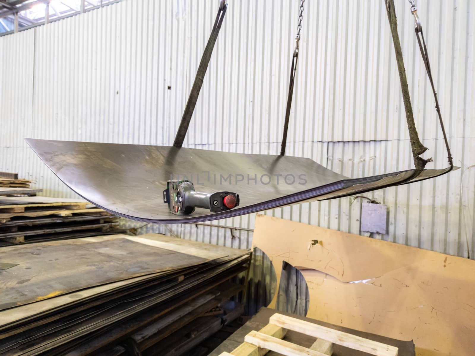 a stack of sheet metal hanging from tearing slings with crane remote control device.