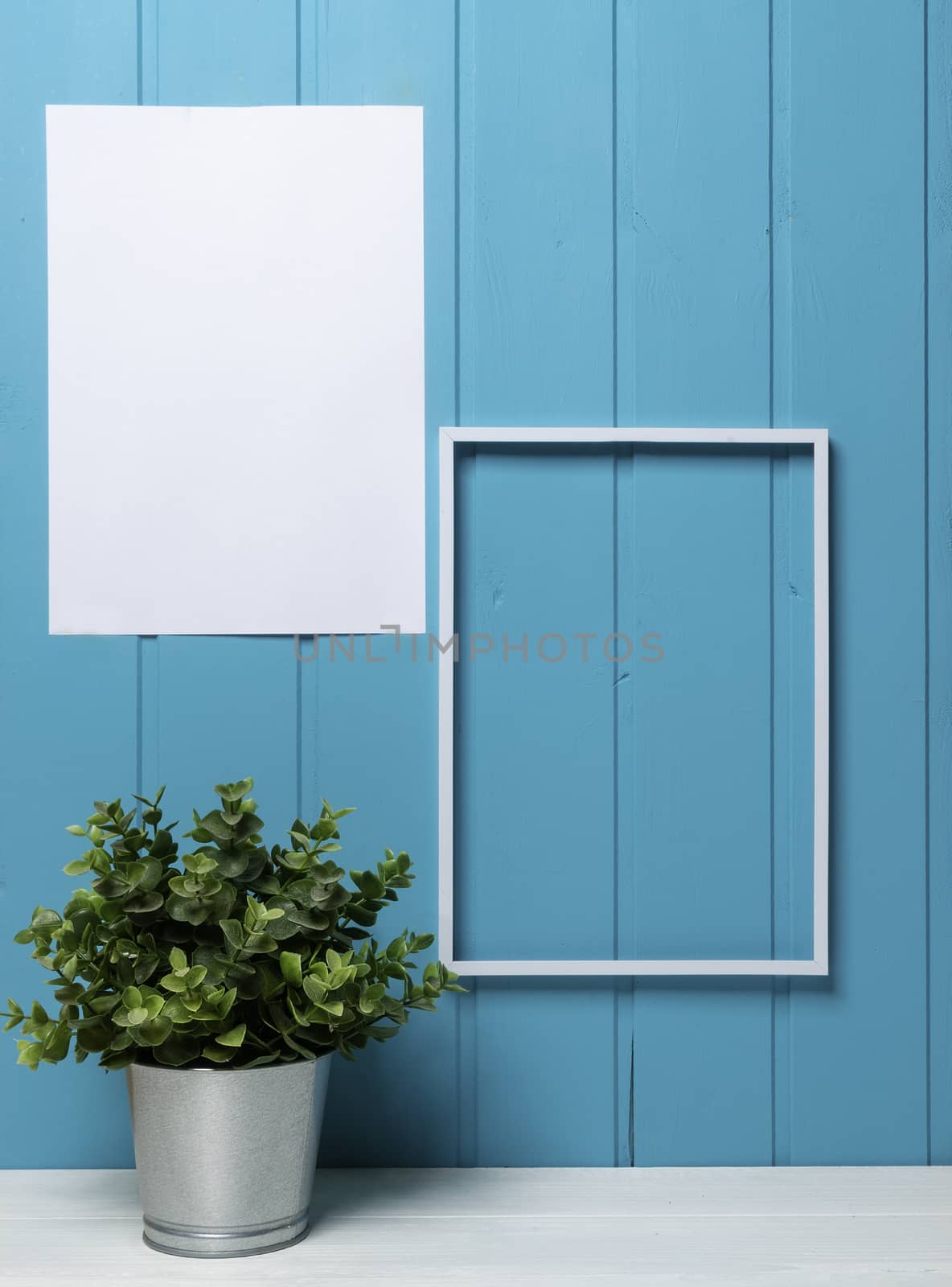 one blank black frame and a plant pot on the table with a blue wood background