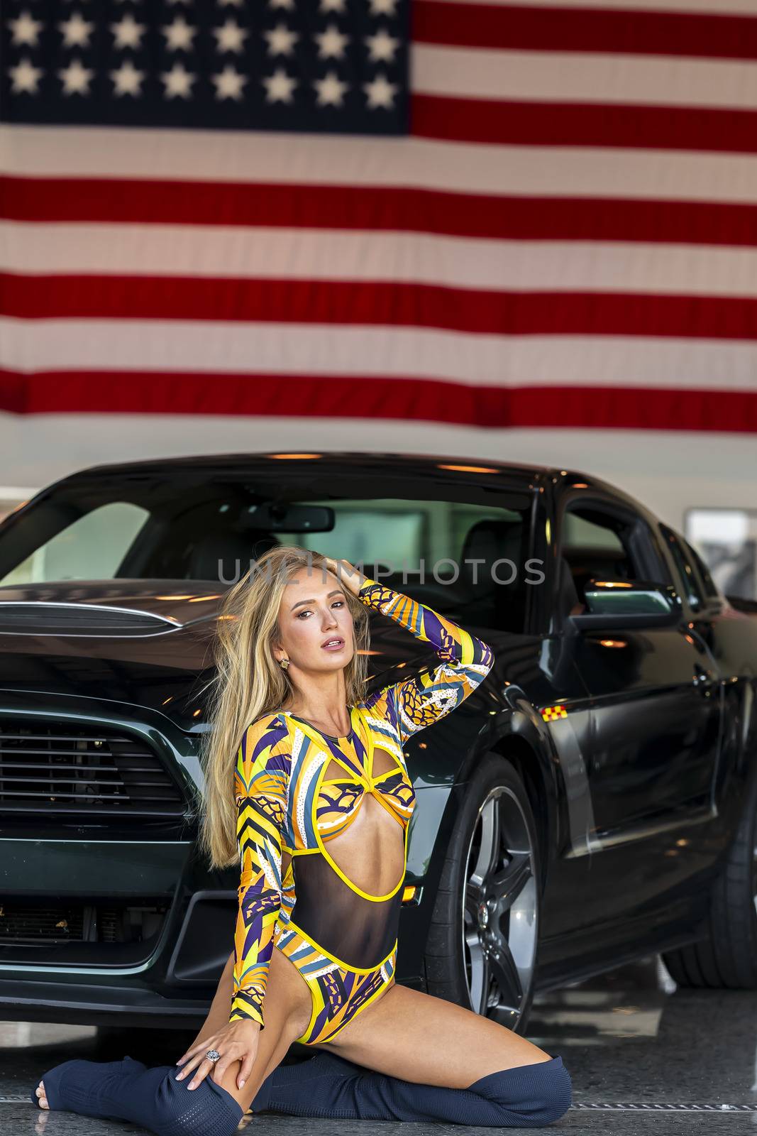 A gorgeous blonde model poses with an American muscle car inside an aircraft hangar