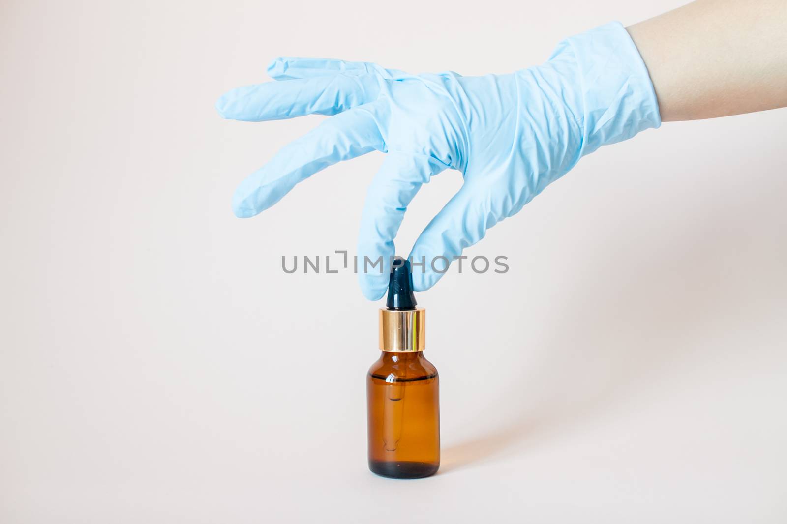 Bottles with serum for the face in his hands in protective medical rubber gloves on a light background. Beauty industry.