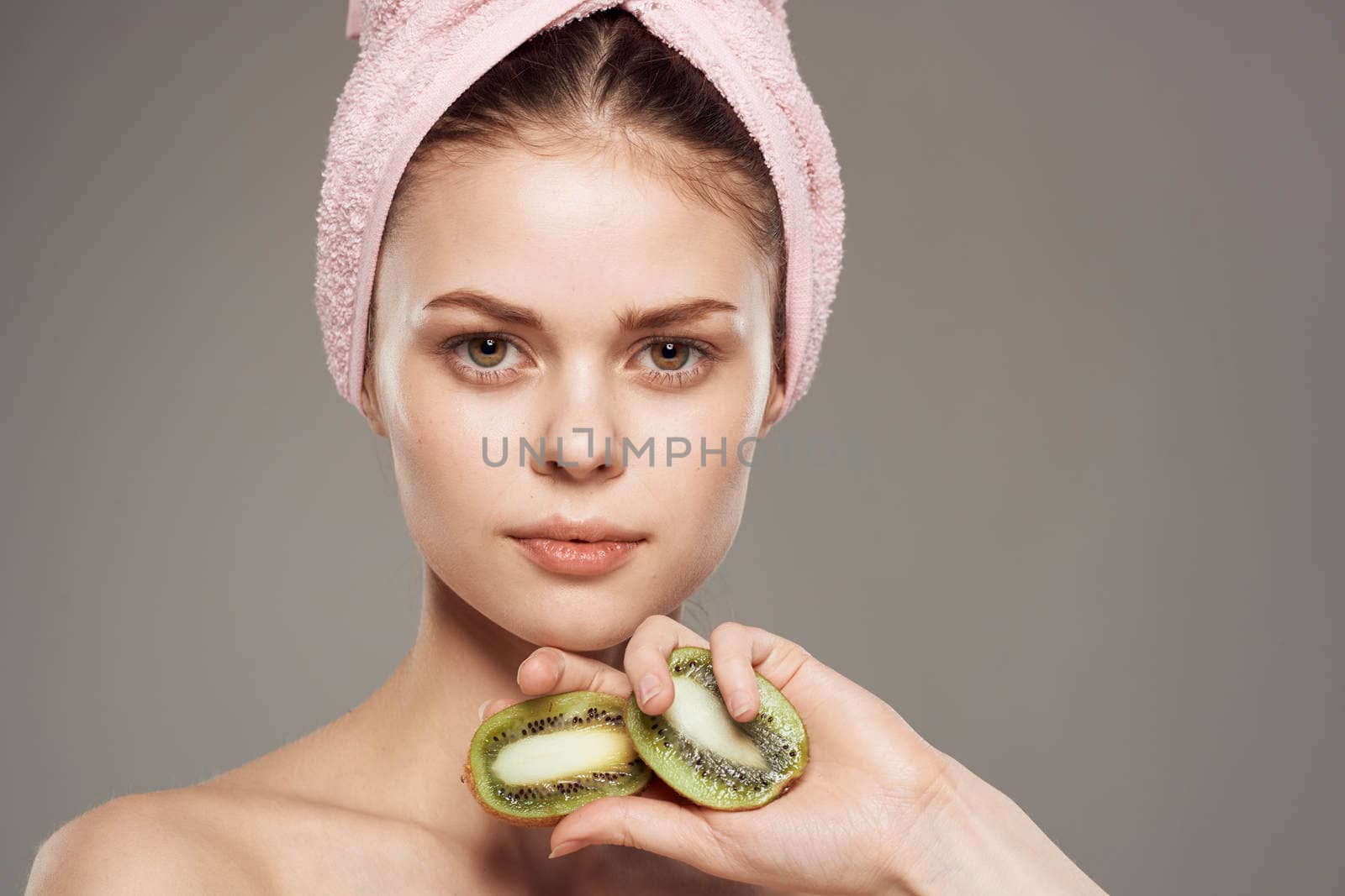 woman with pink towel on her head bare shoulders cropped view of kiwi fruit in health hand by SHOTPRIME